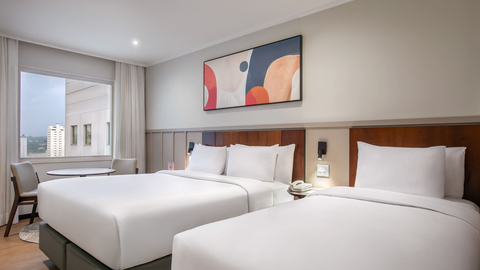 Hotel room with two queen beds, modern art, and a city window view.