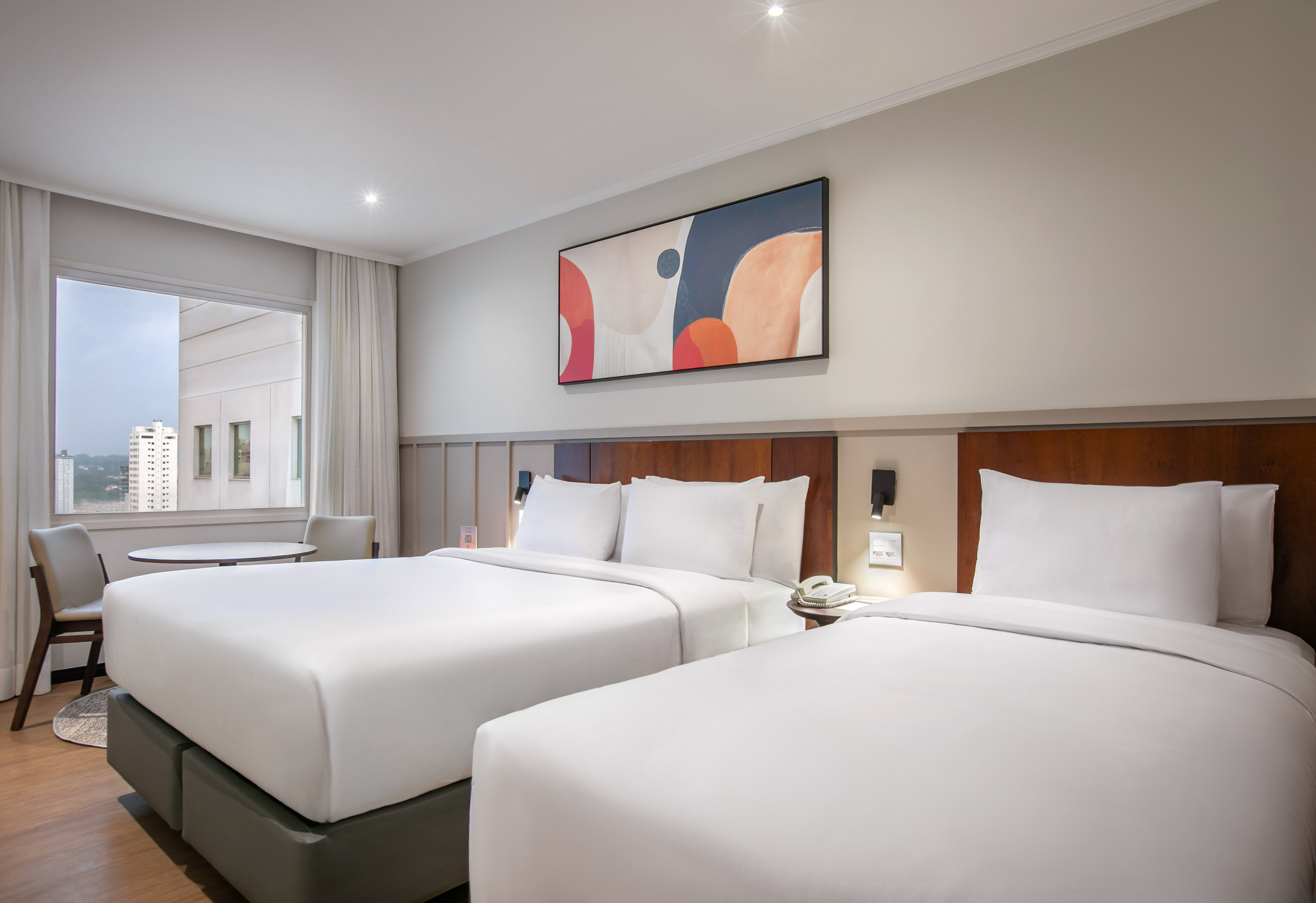 Hotel room with two queen beds, modern art, and a city window view.