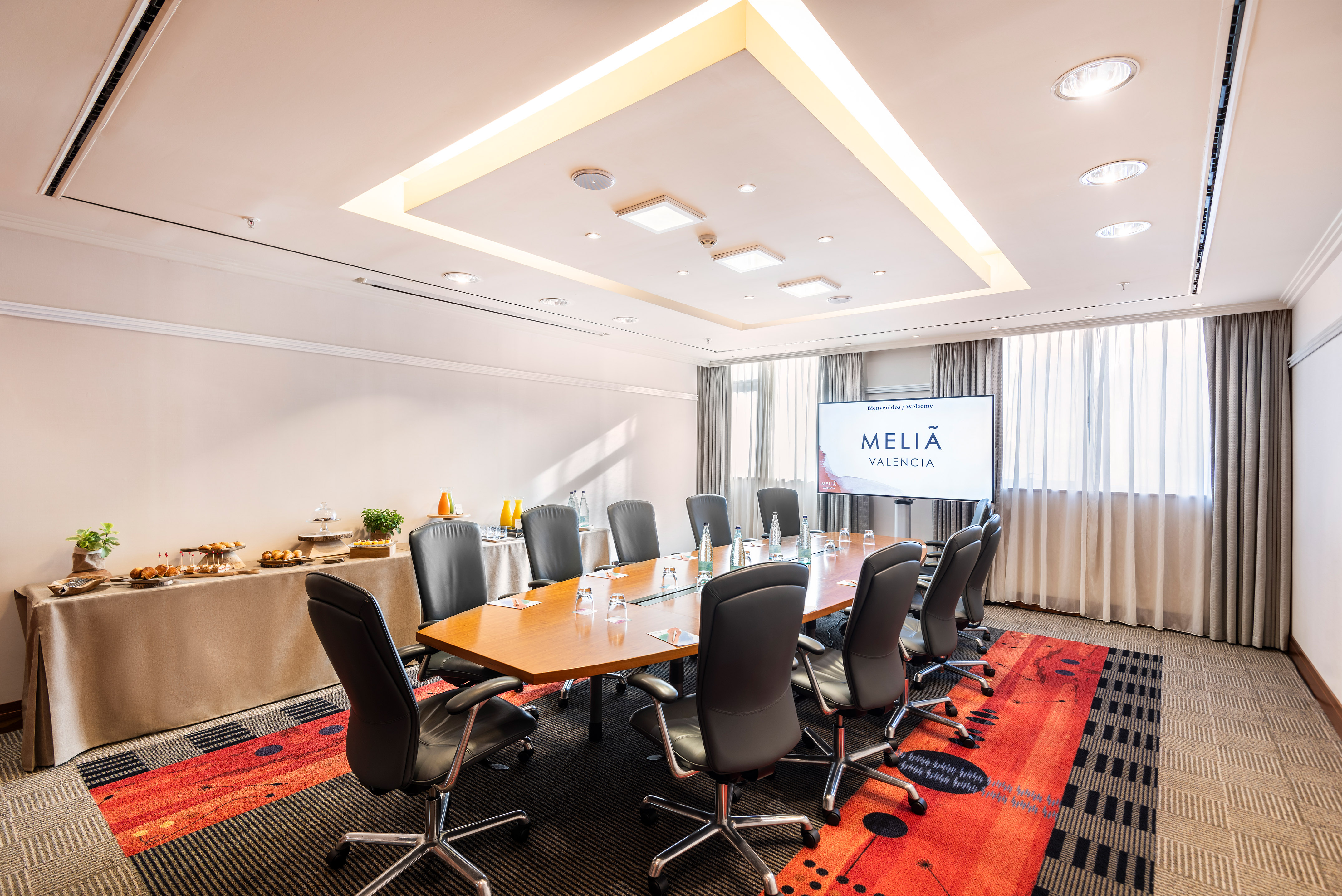 Meliã Valencia meeting room with large table, black chairs, TV, and buffet.