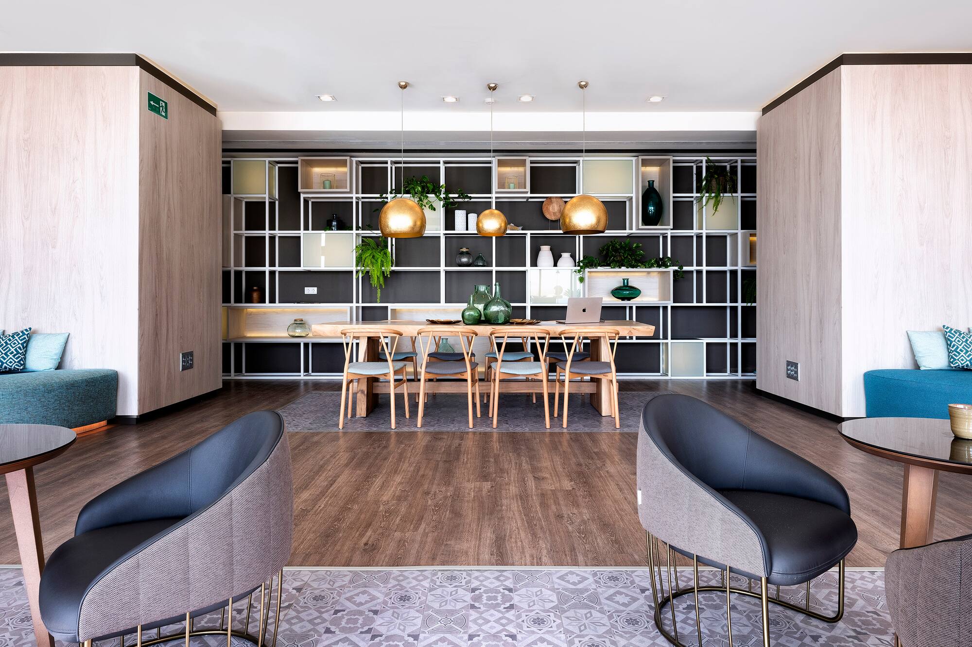 Modern hotel lounge with wooden communal table and golden pendant lights.
