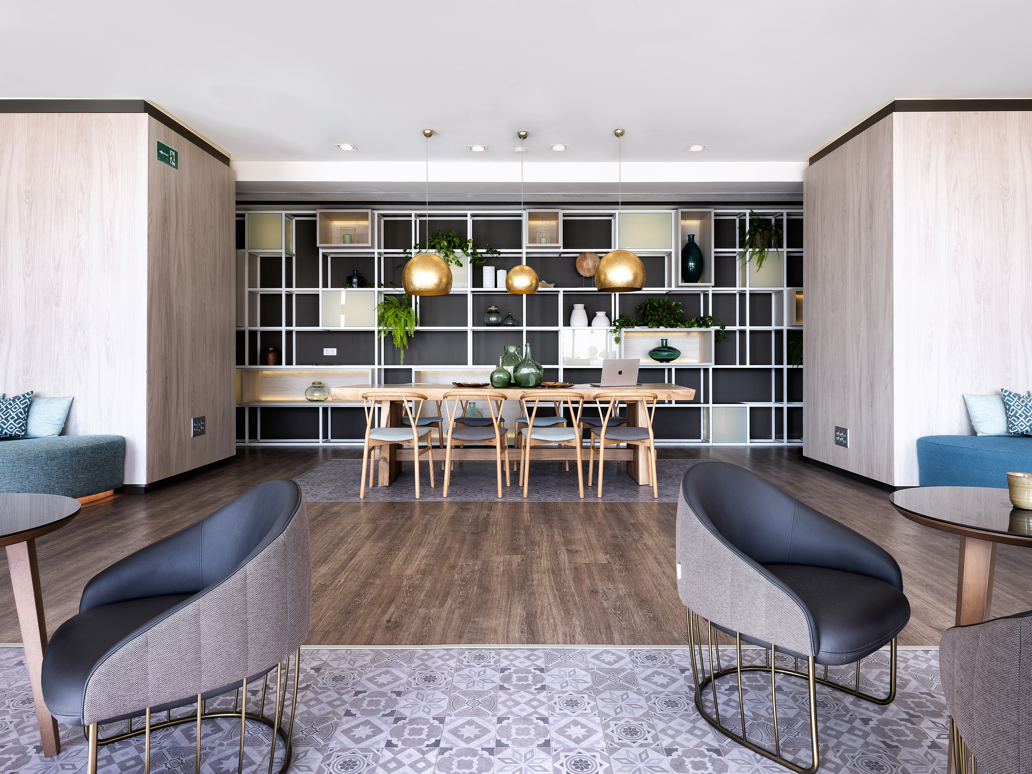 Modern hotel lounge with wooden communal table and golden pendant lights.