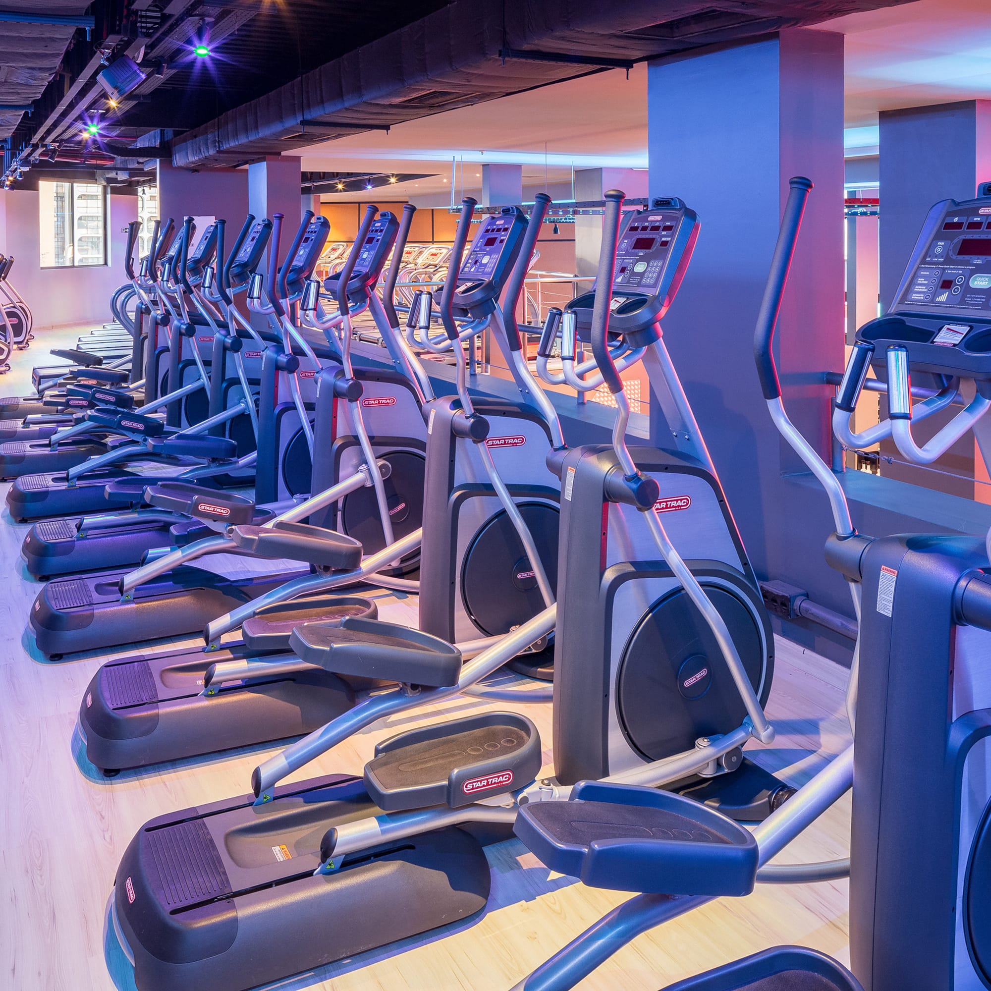 Modern gym with multiple Star Trac elliptical machines and vibrant lighting.