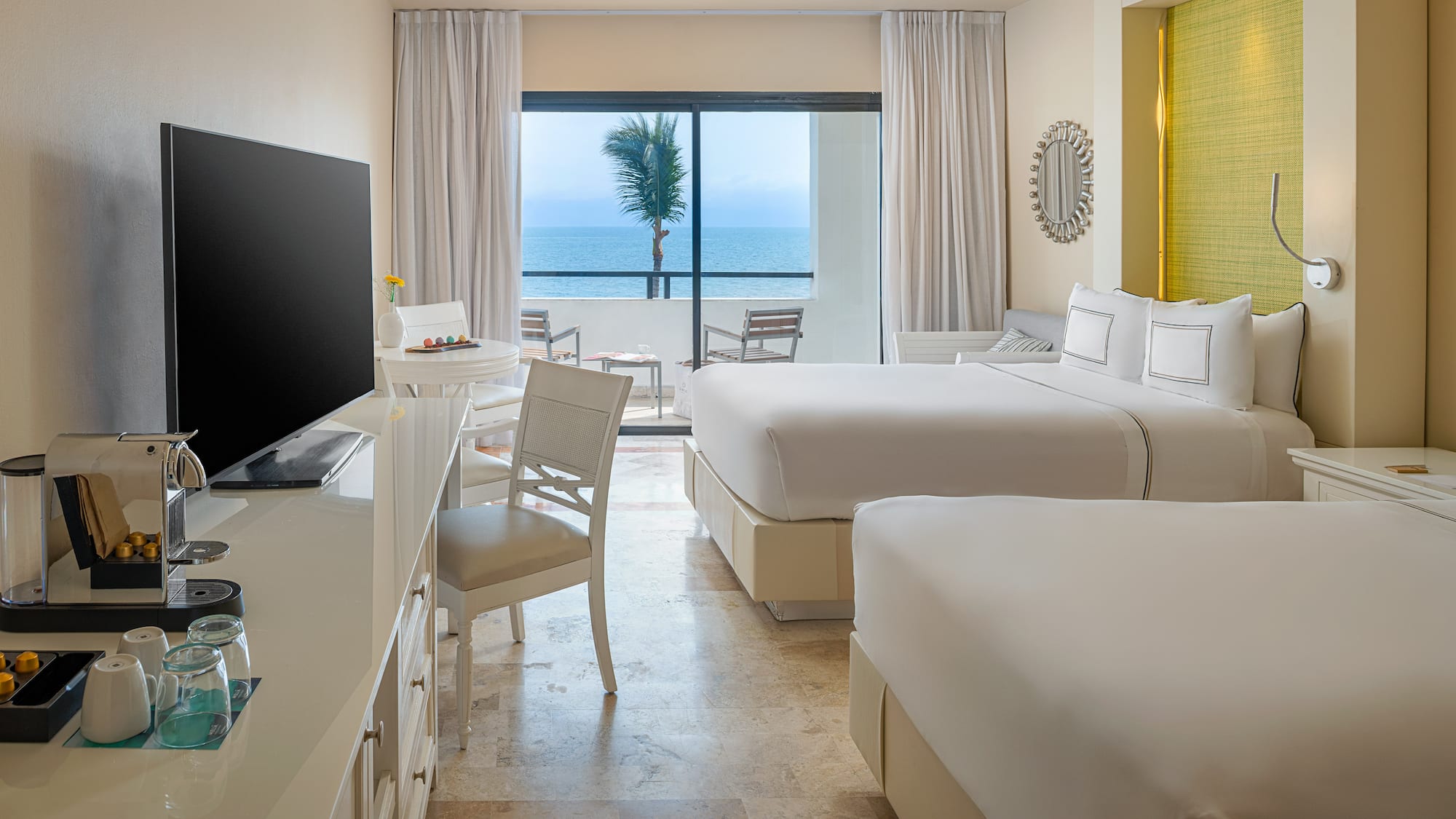 Hotel room with ocean view, two beds, balcony, and coffee machine.