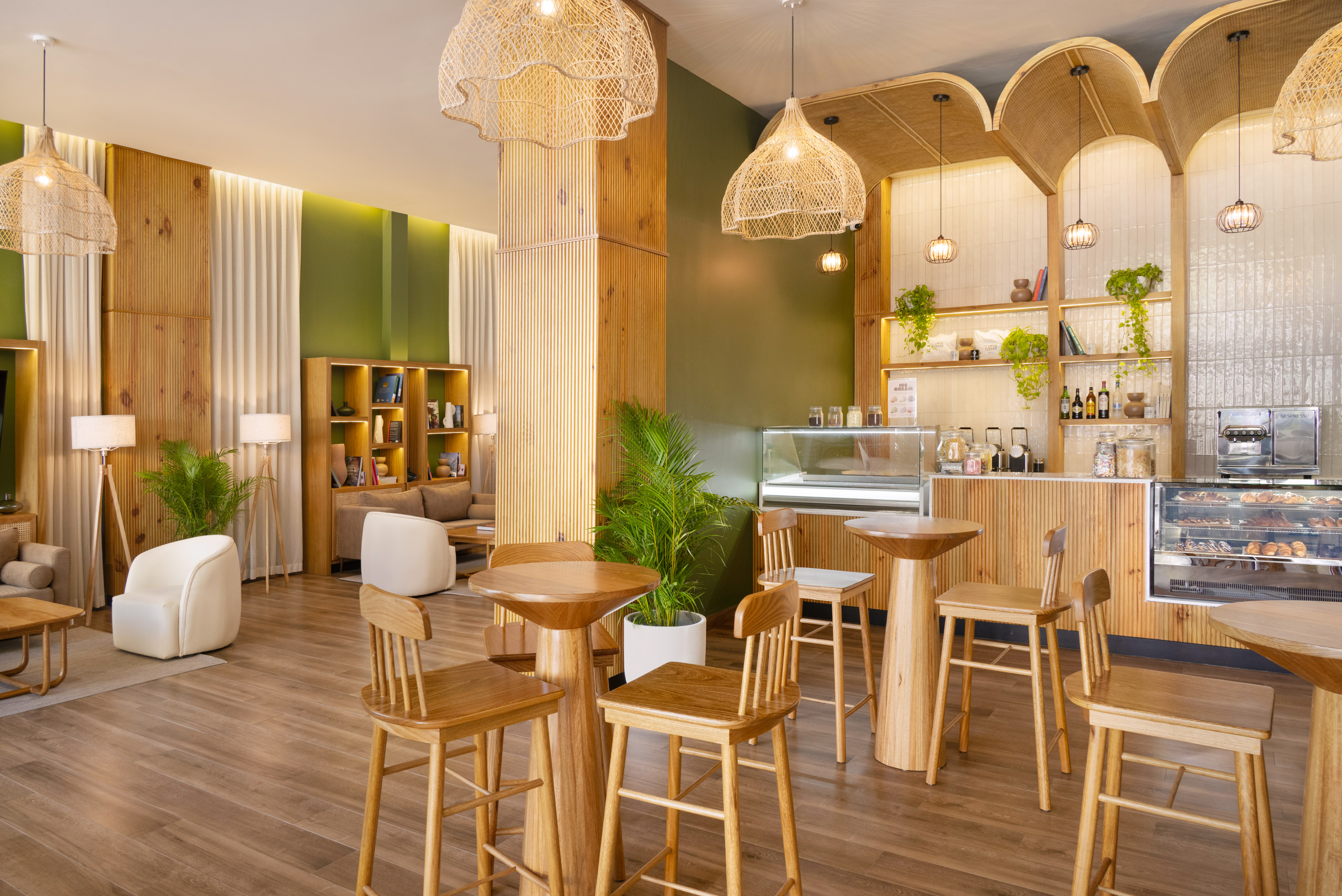 Warm cafe interior with wood furniture, green walls, wicker lights, and bakery.