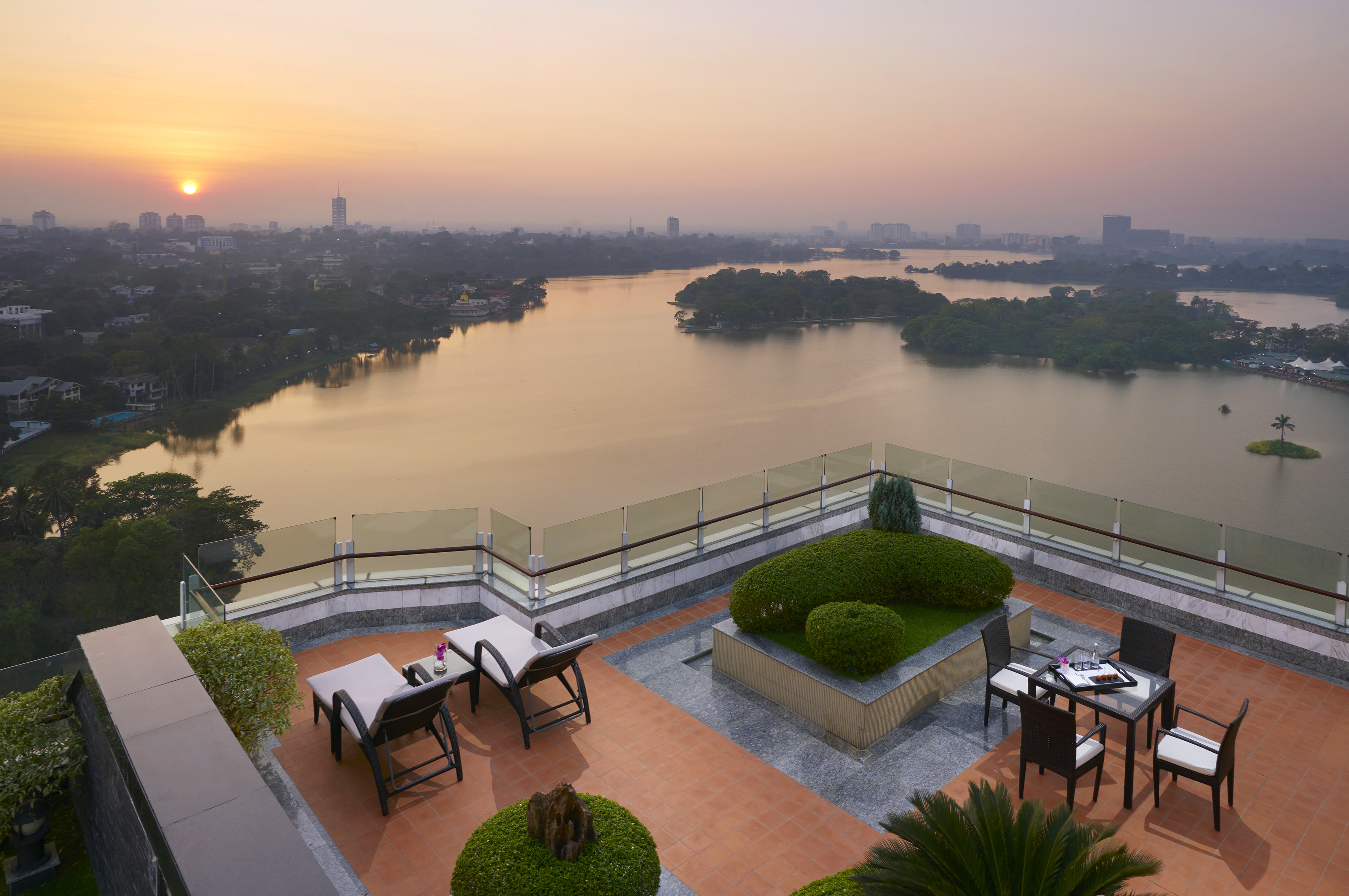 Rooftop terrace with panoramic lake and city view at sunset, outdoor seating.