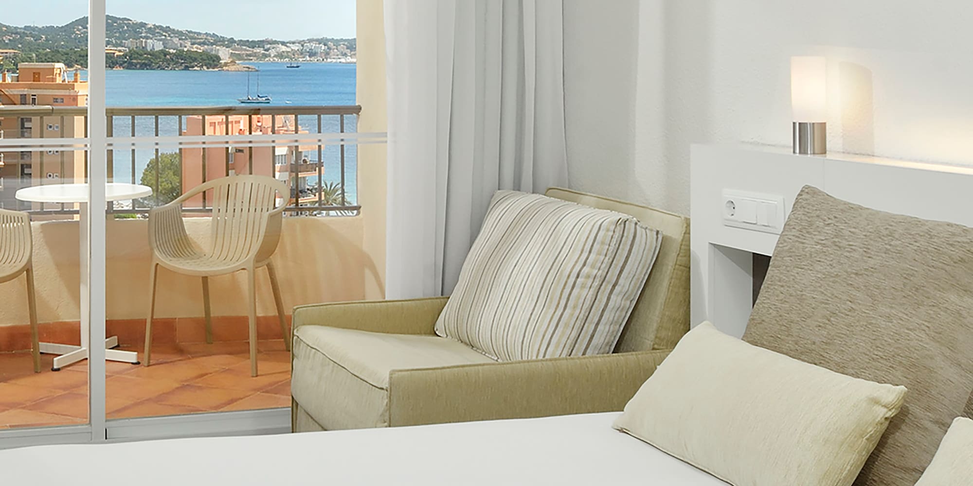 a bed with pillows and a chair in a room with a balcony overlooking the water