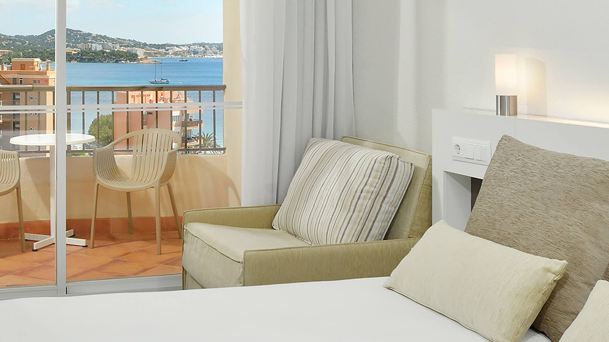 a bed with pillows and a chair in a room with a balcony overlooking the water