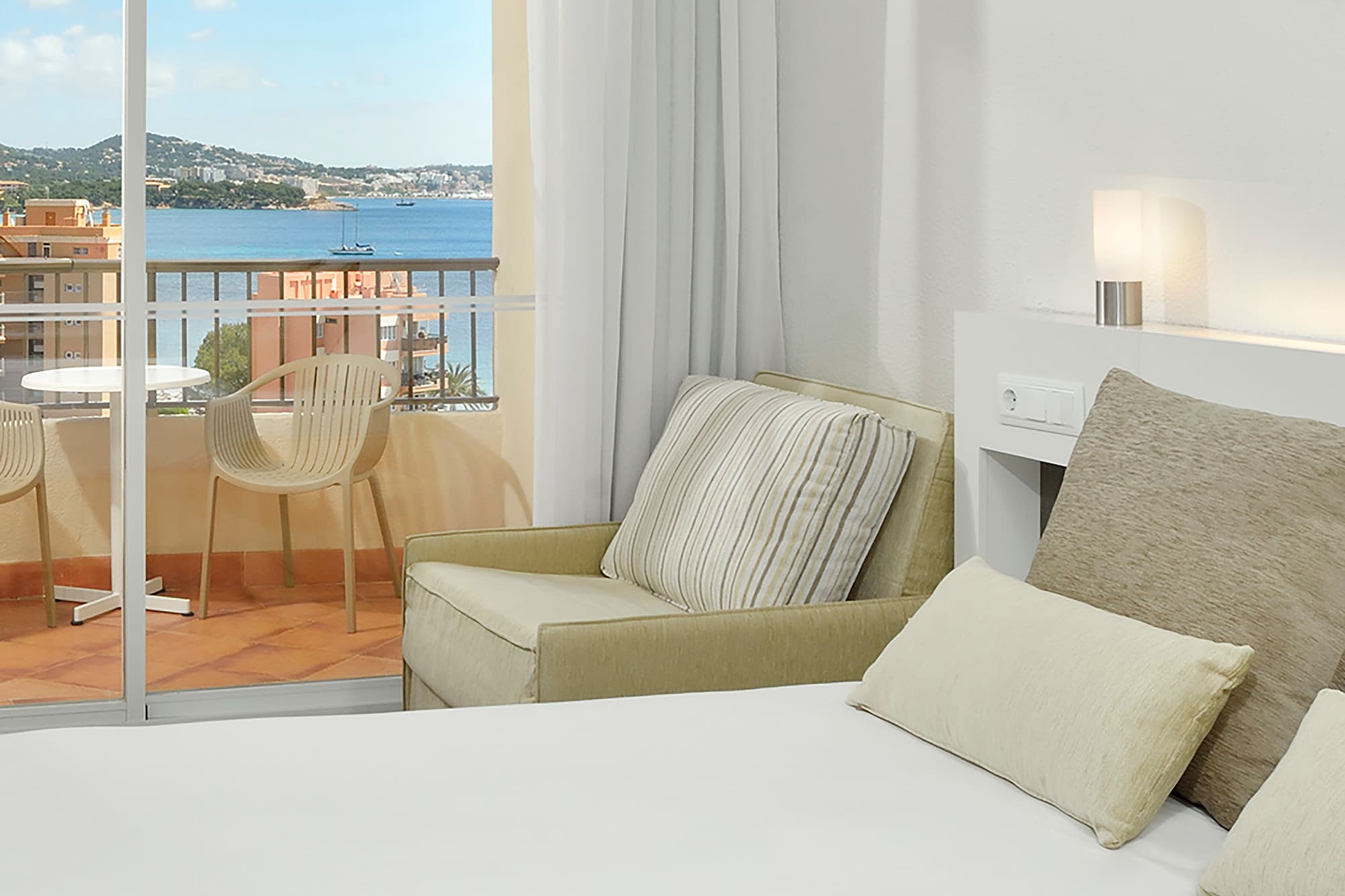 a bed with pillows and a chair in a room with a balcony overlooking the water
