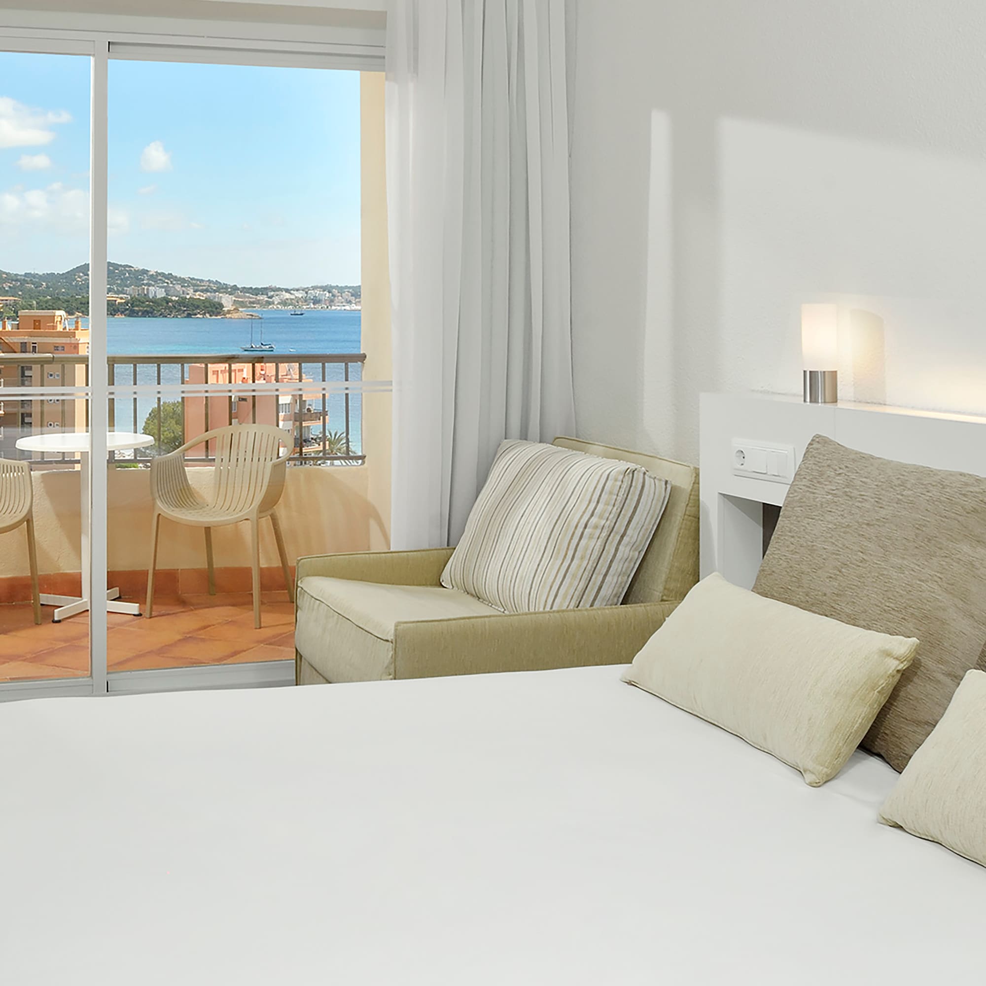 a bed with pillows and a chair in a room with a balcony overlooking the water