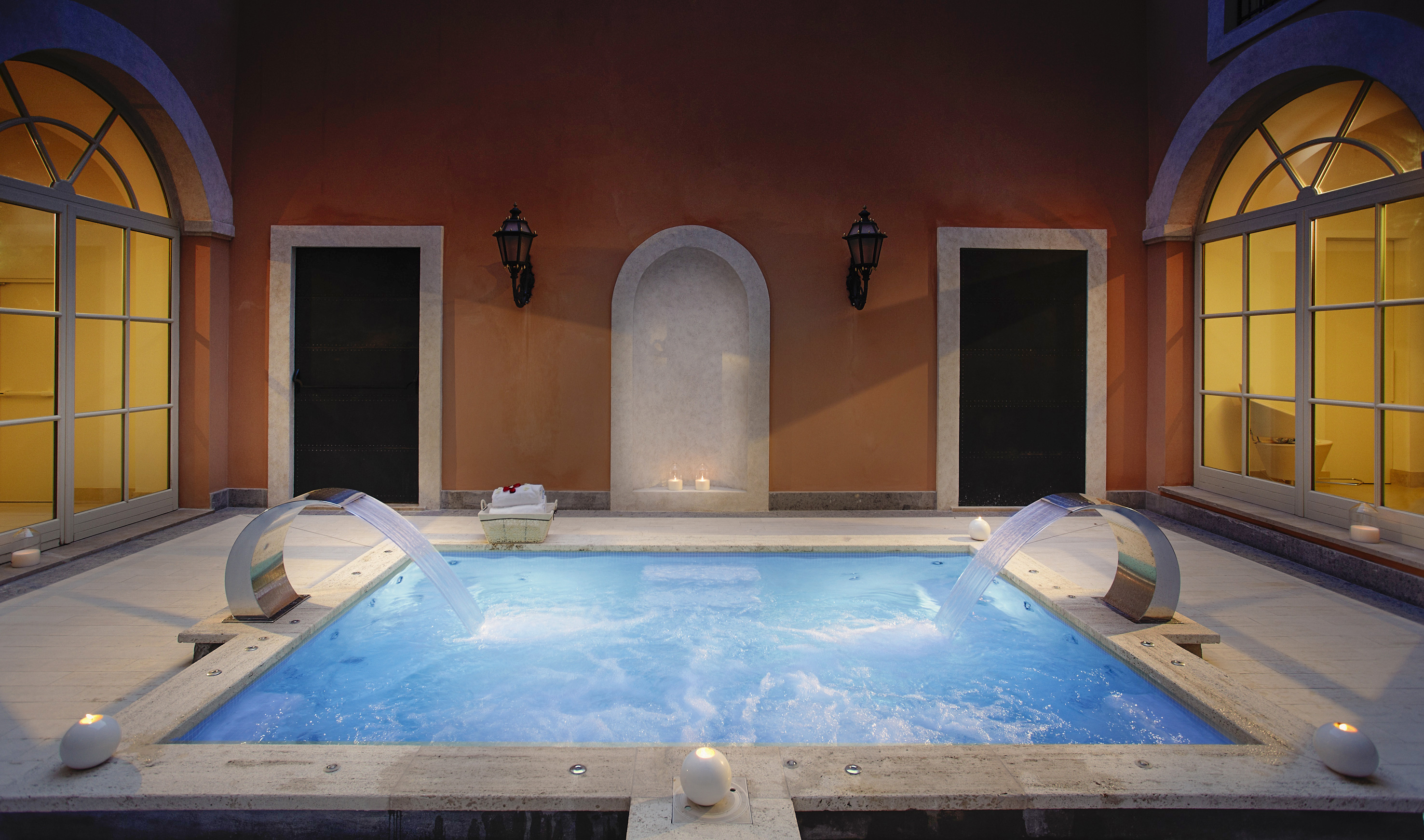 Luxurious indoor spa pool with waterfalls, warm lighting, and terracotta walls.