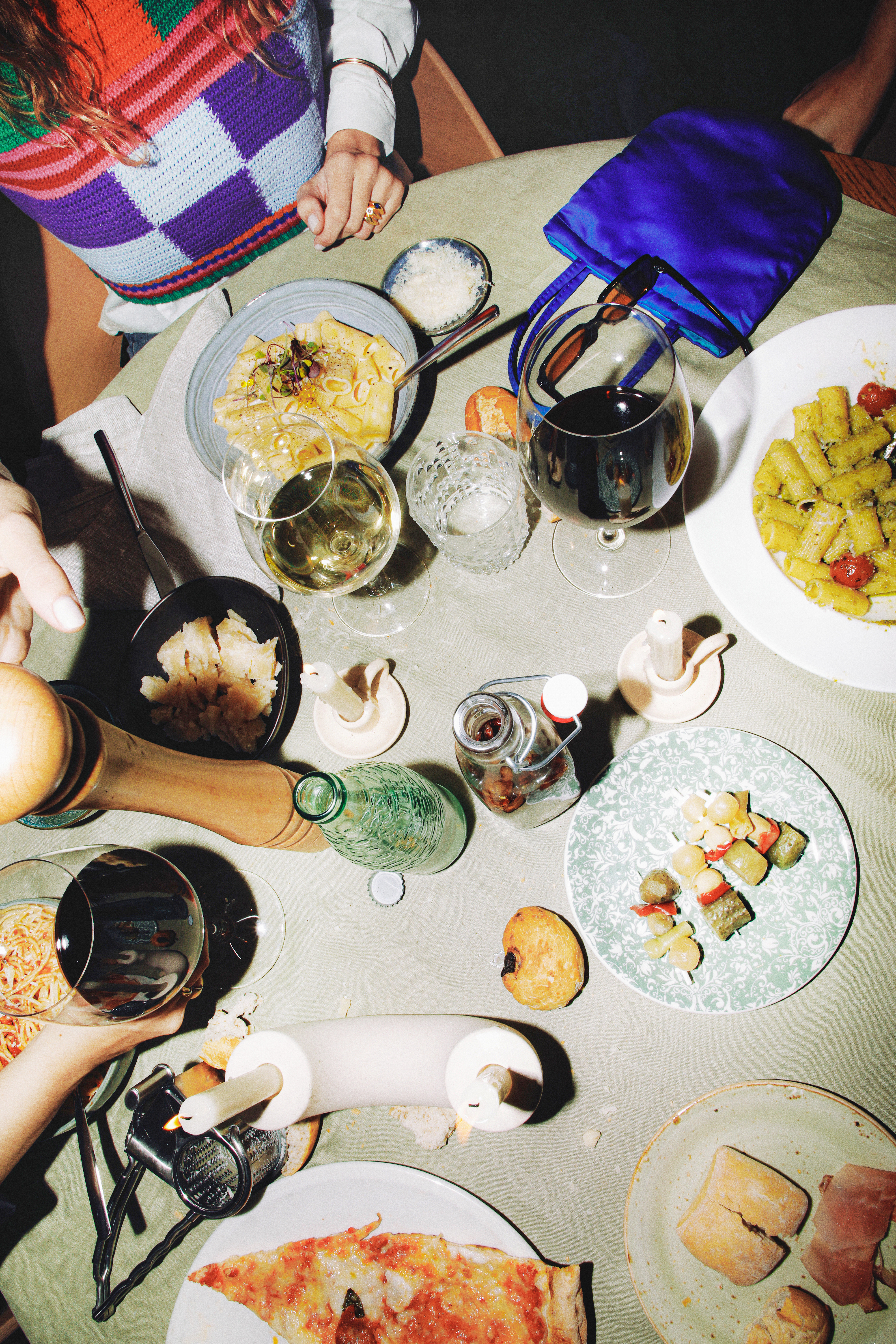 Italian dinner table with pasta, pizza, wine, cheese, and hands reaching for food.