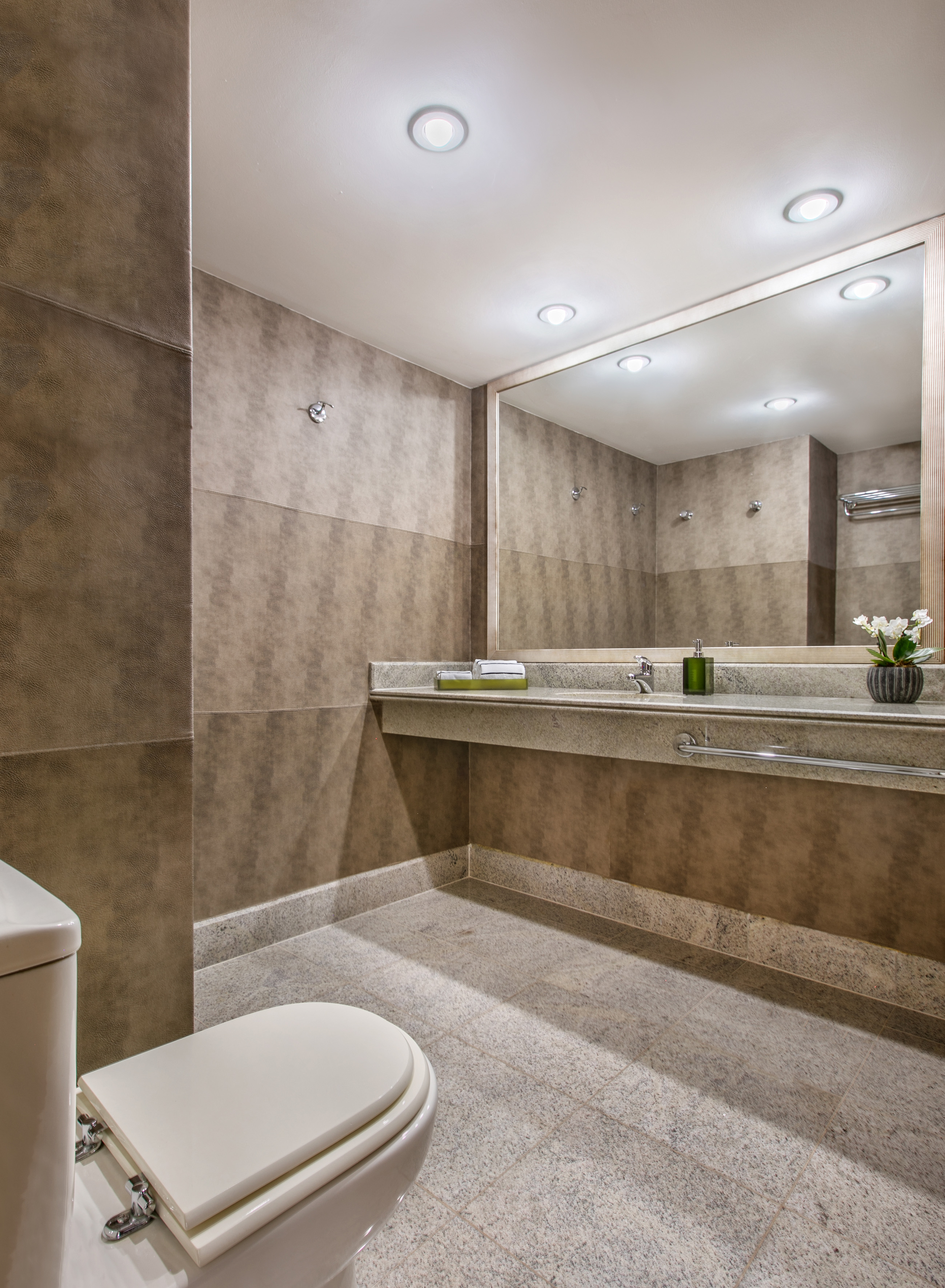 Brown tiled modern bathroom with granite vanity, mirror, and toilet.