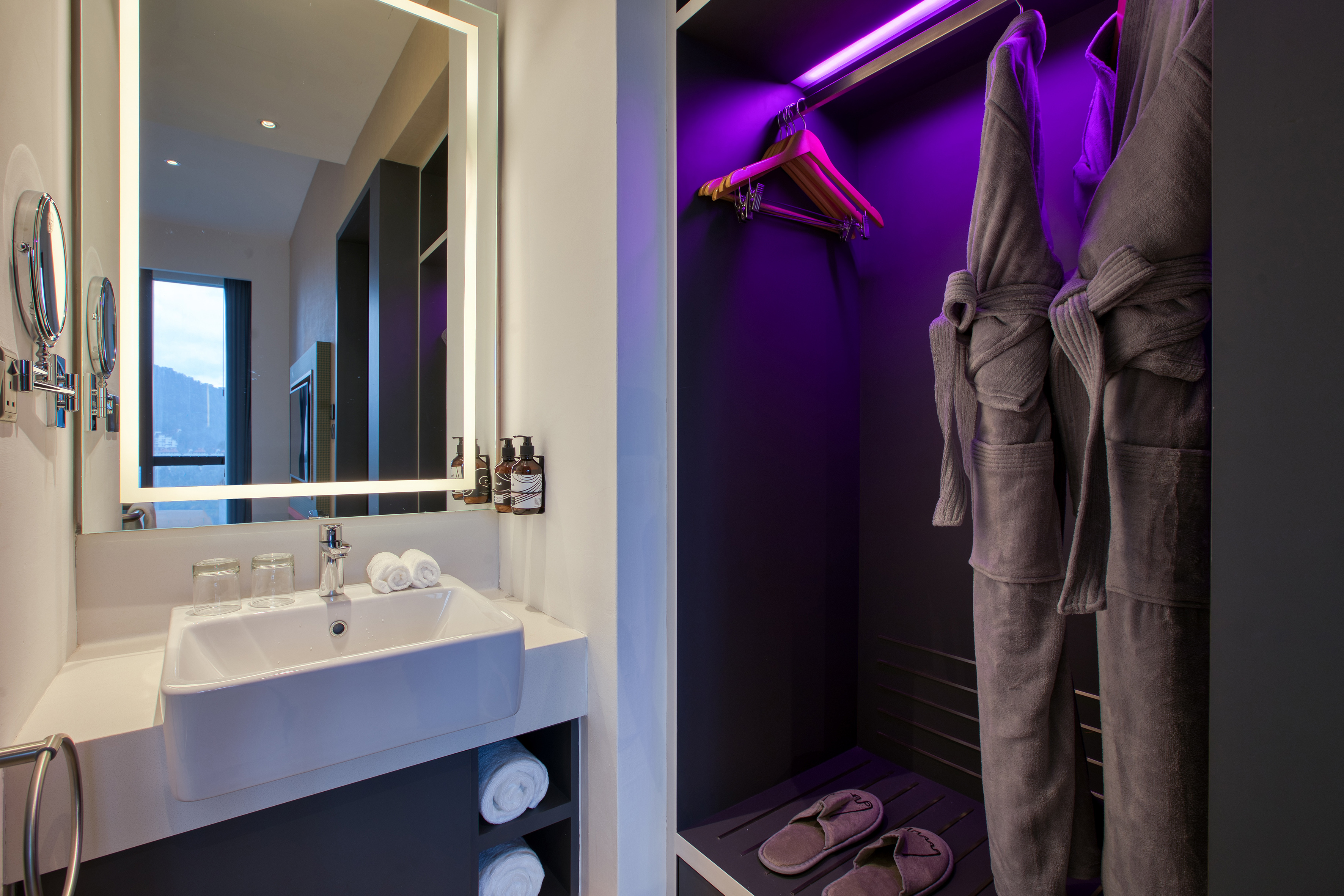 Hotel bathroom vanity, lighted mirror, bathrobes, slippers, purple closet light.