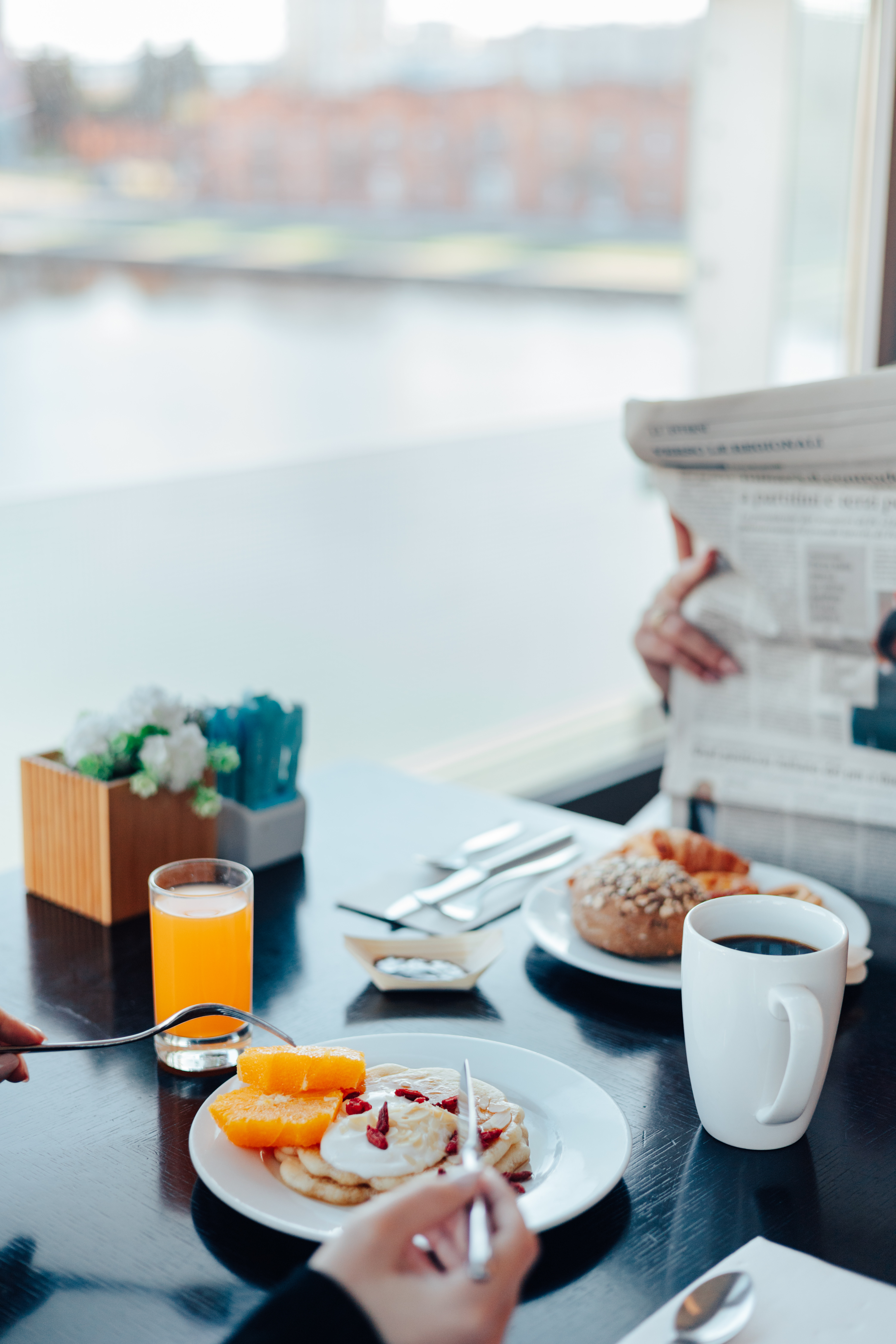 Hotel breakfast with pancakes, orange juice, coffee, and newspaper by a window.