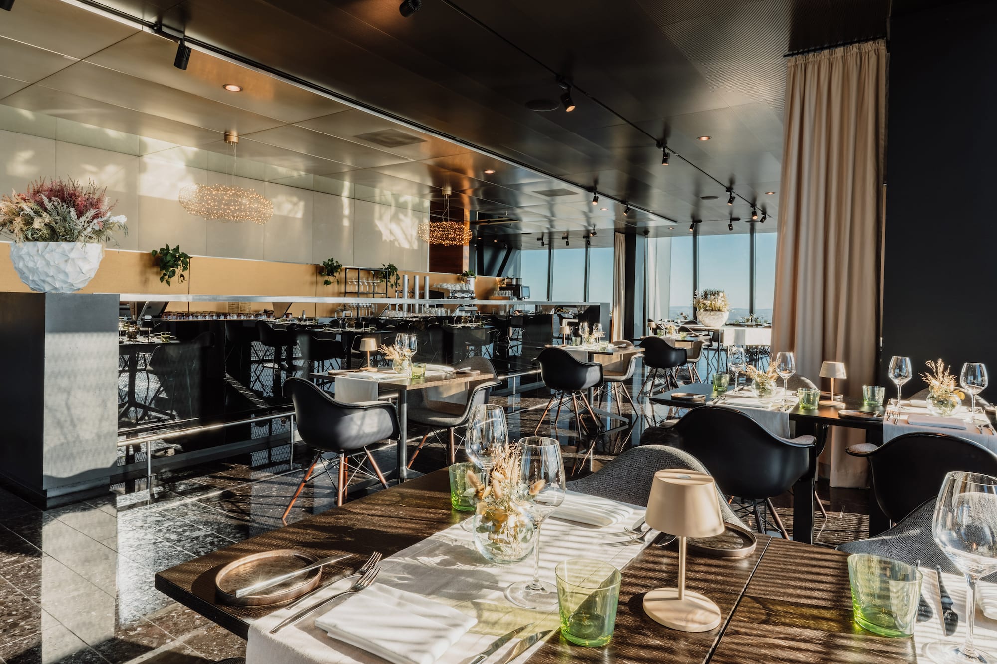 Elegant modern restaurant interior with bar, set tables, and panoramic views.