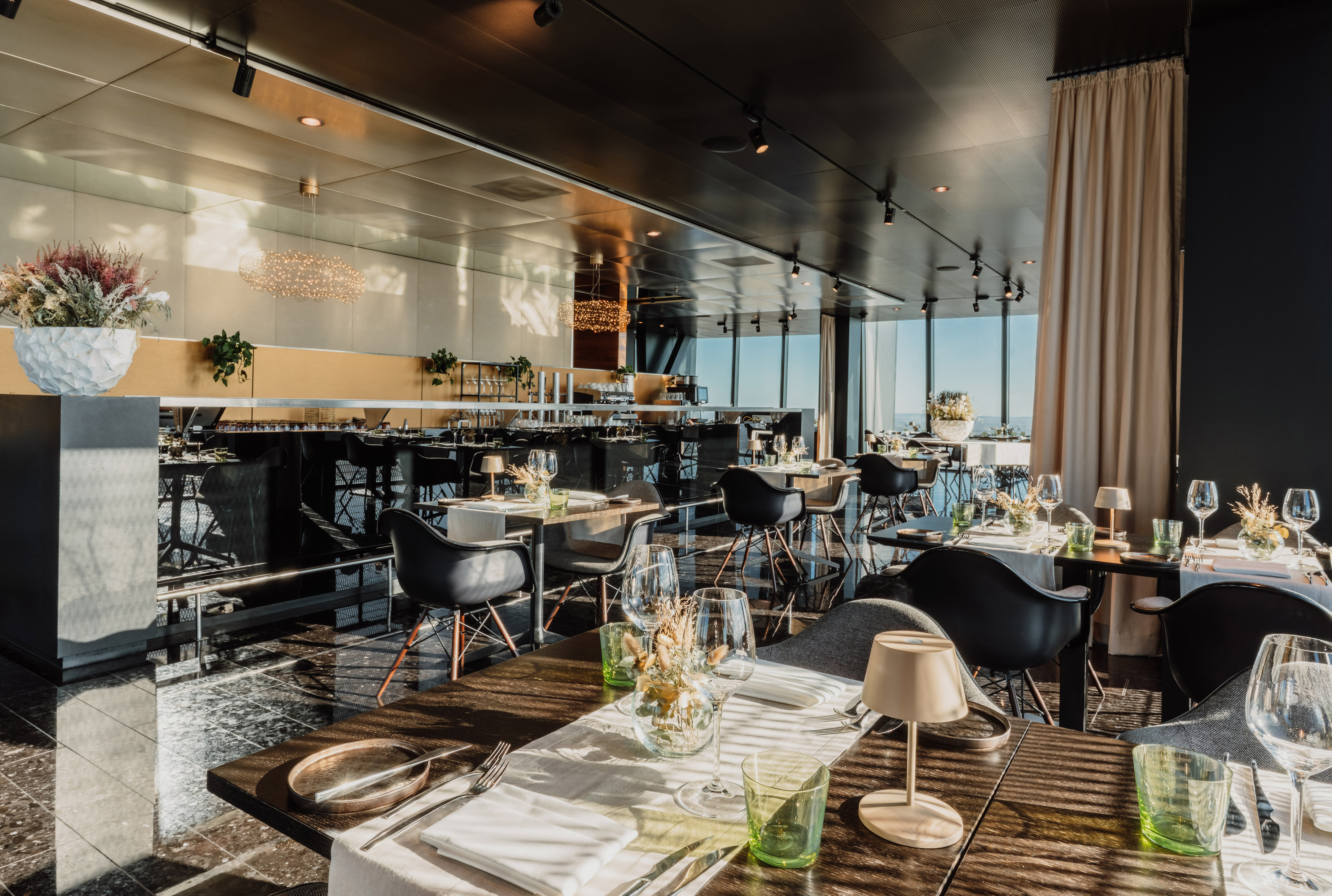 Elegant modern restaurant interior with bar, set tables, and panoramic views.
