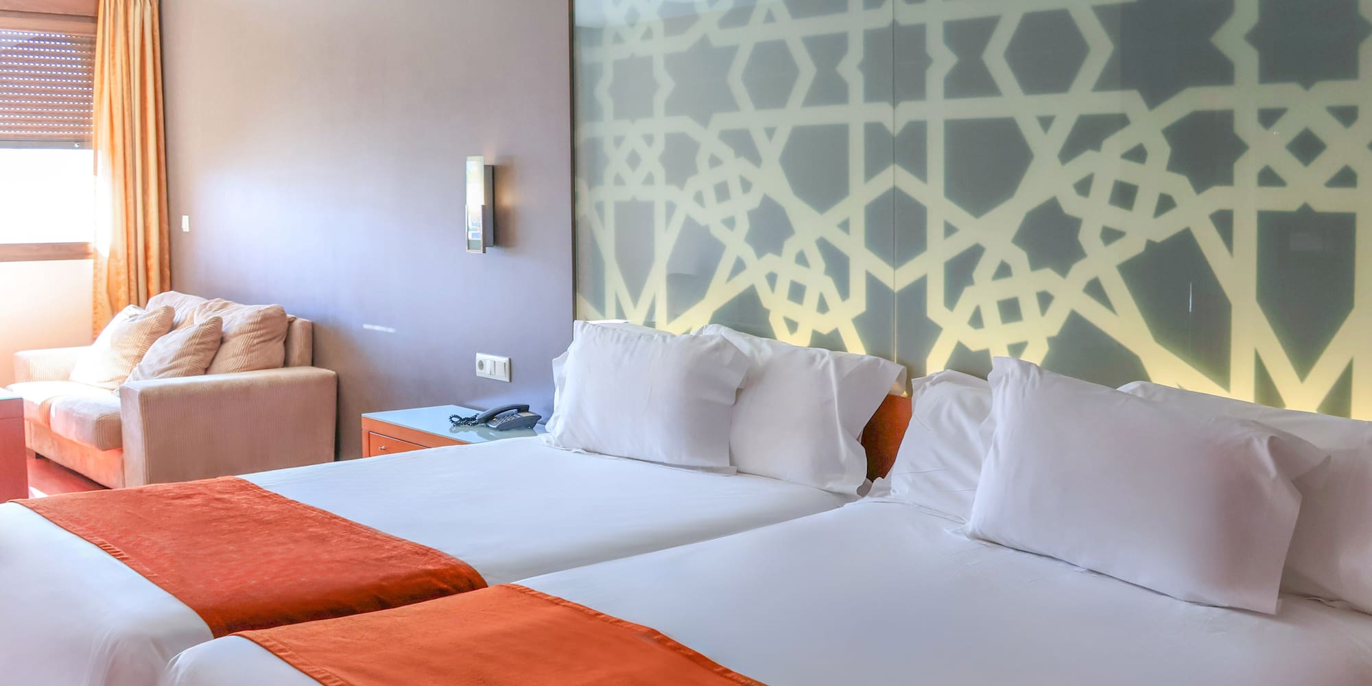 Hotel room with twin beds, orange runners, and geometric headboard.