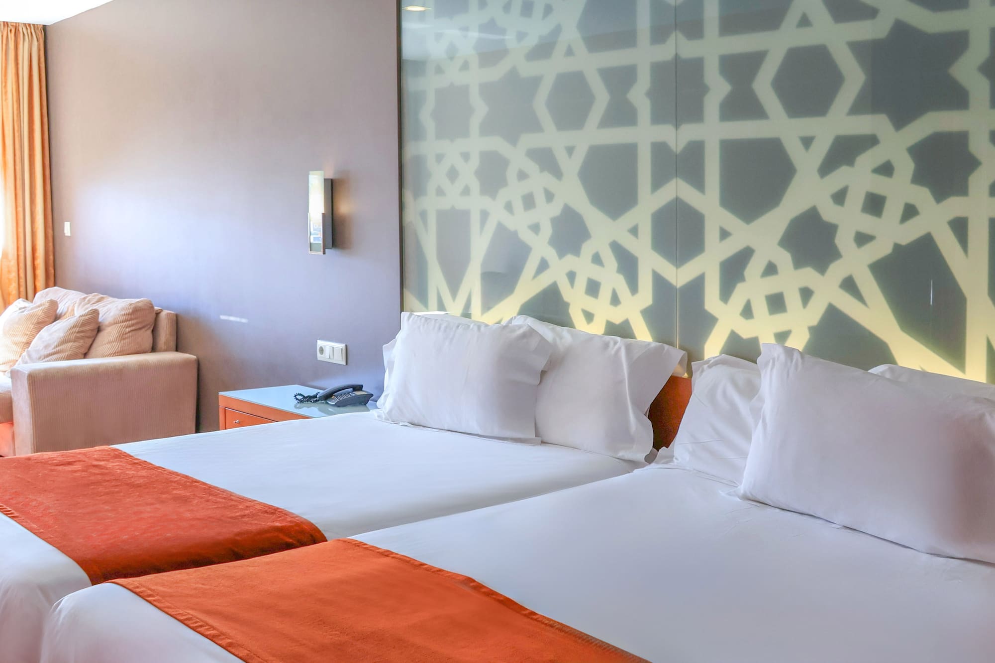 Hotel room with twin beds, orange runners, and geometric headboard.