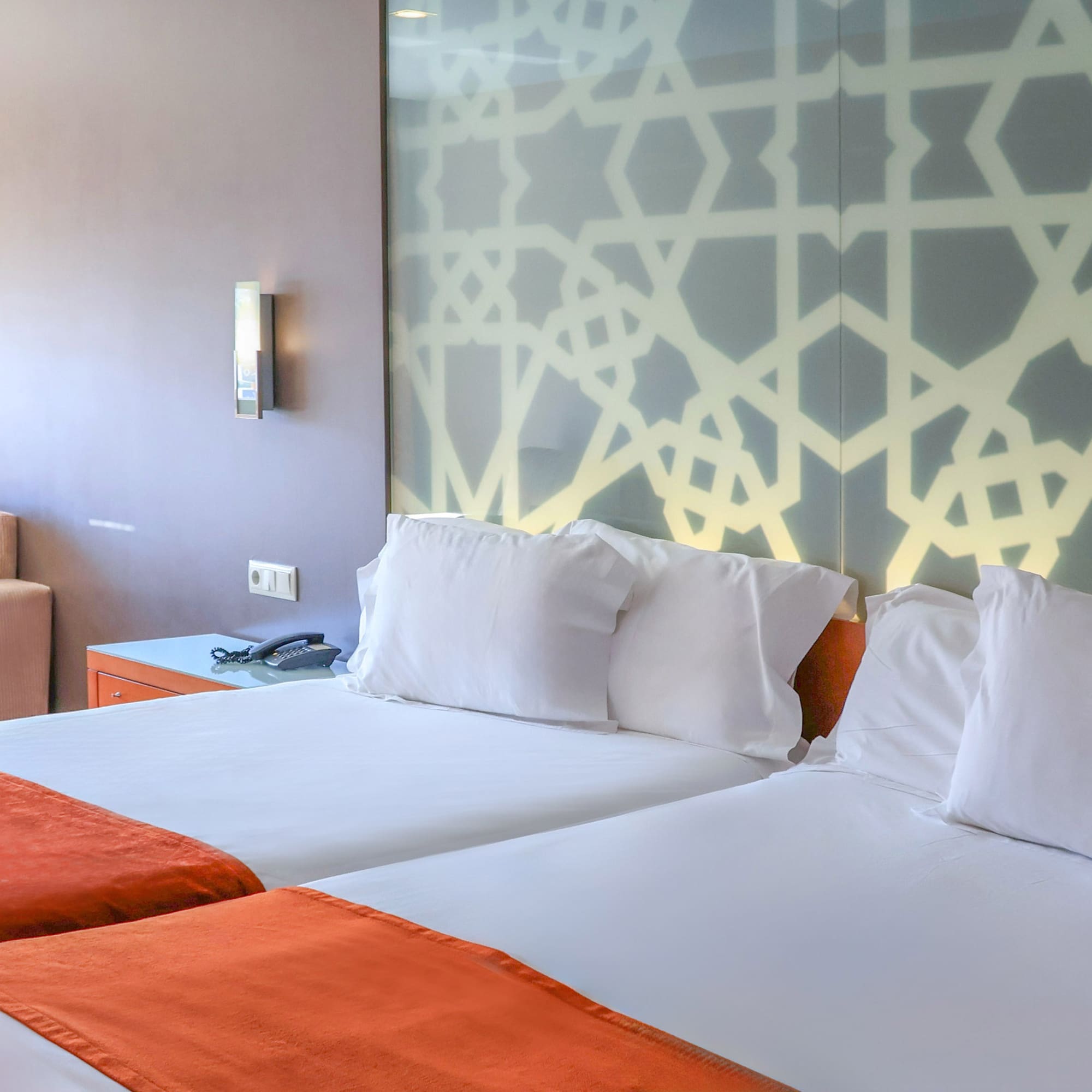 Hotel room with twin beds, orange runners, and geometric headboard.