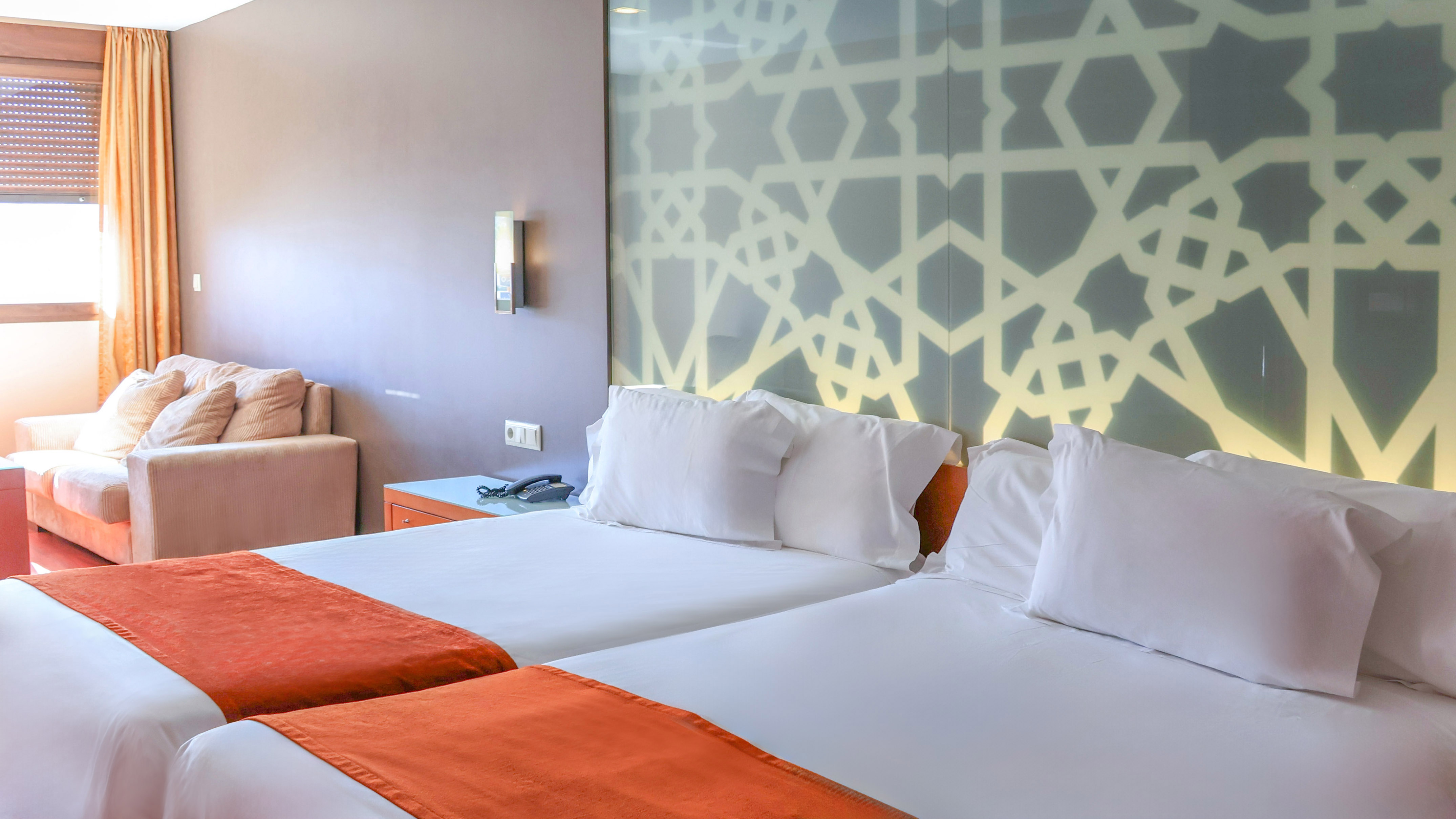 Hotel room with twin beds, orange runners, and geometric headboard.