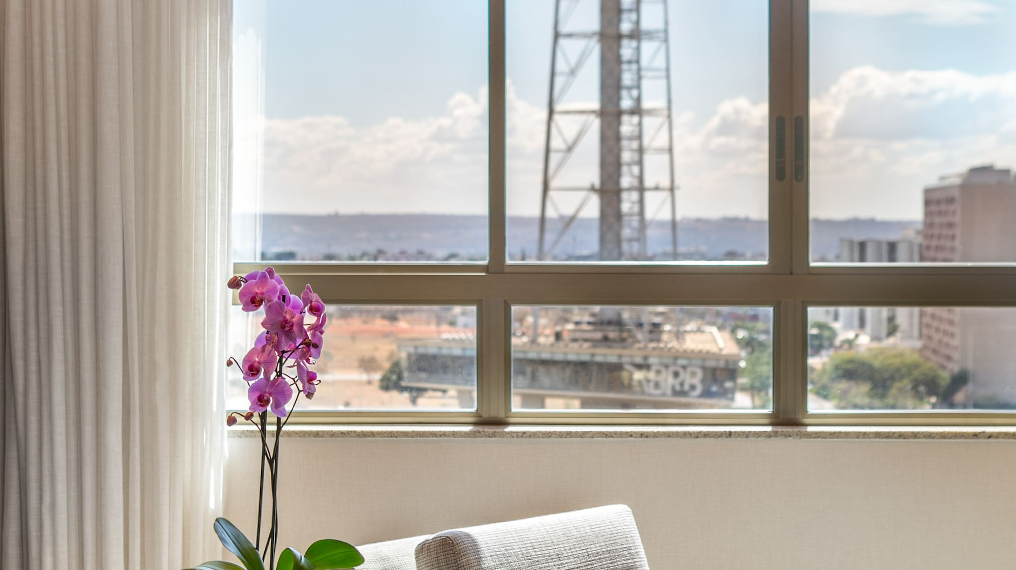 Hotel suite interior with city skyline view, purple orchid, and armchair.