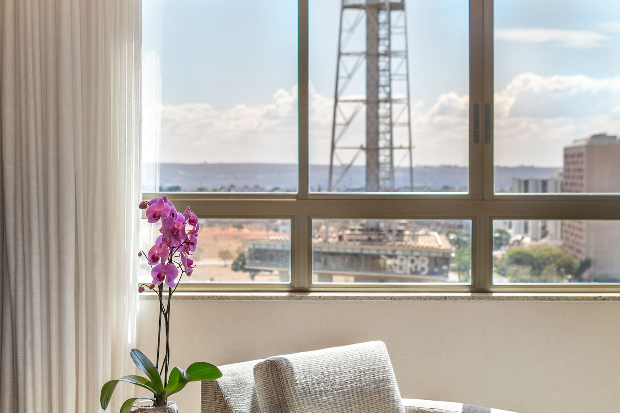 Hotel suite interior with city skyline view, purple orchid, and armchair.