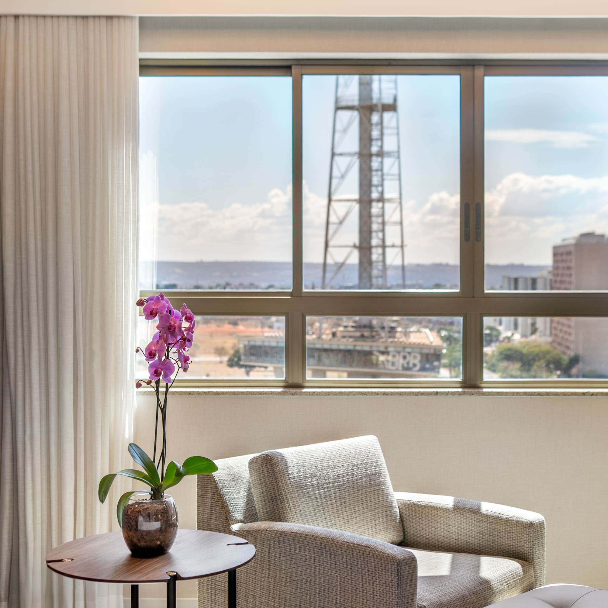 Bright hotel room: city view window, purple orchid, modern armchair.