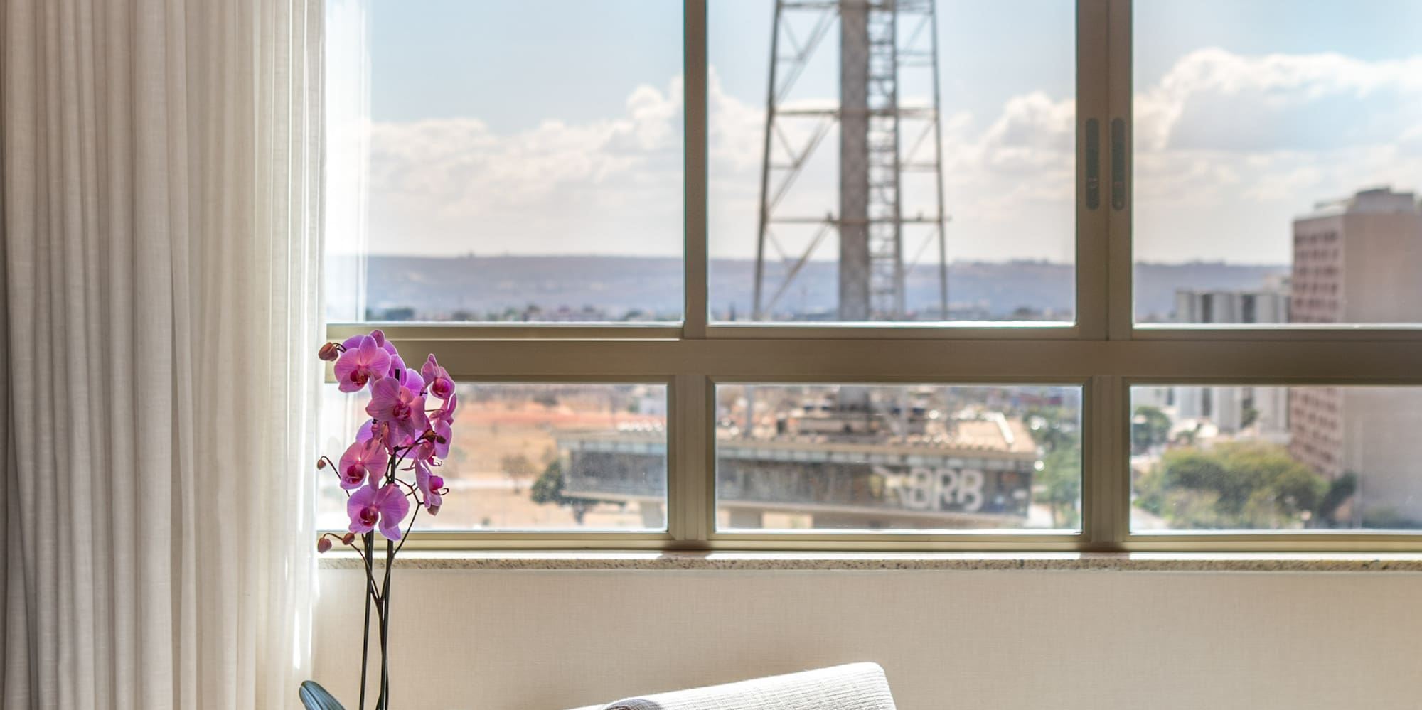 Bright hotel room: city view window, purple orchid, modern armchair.