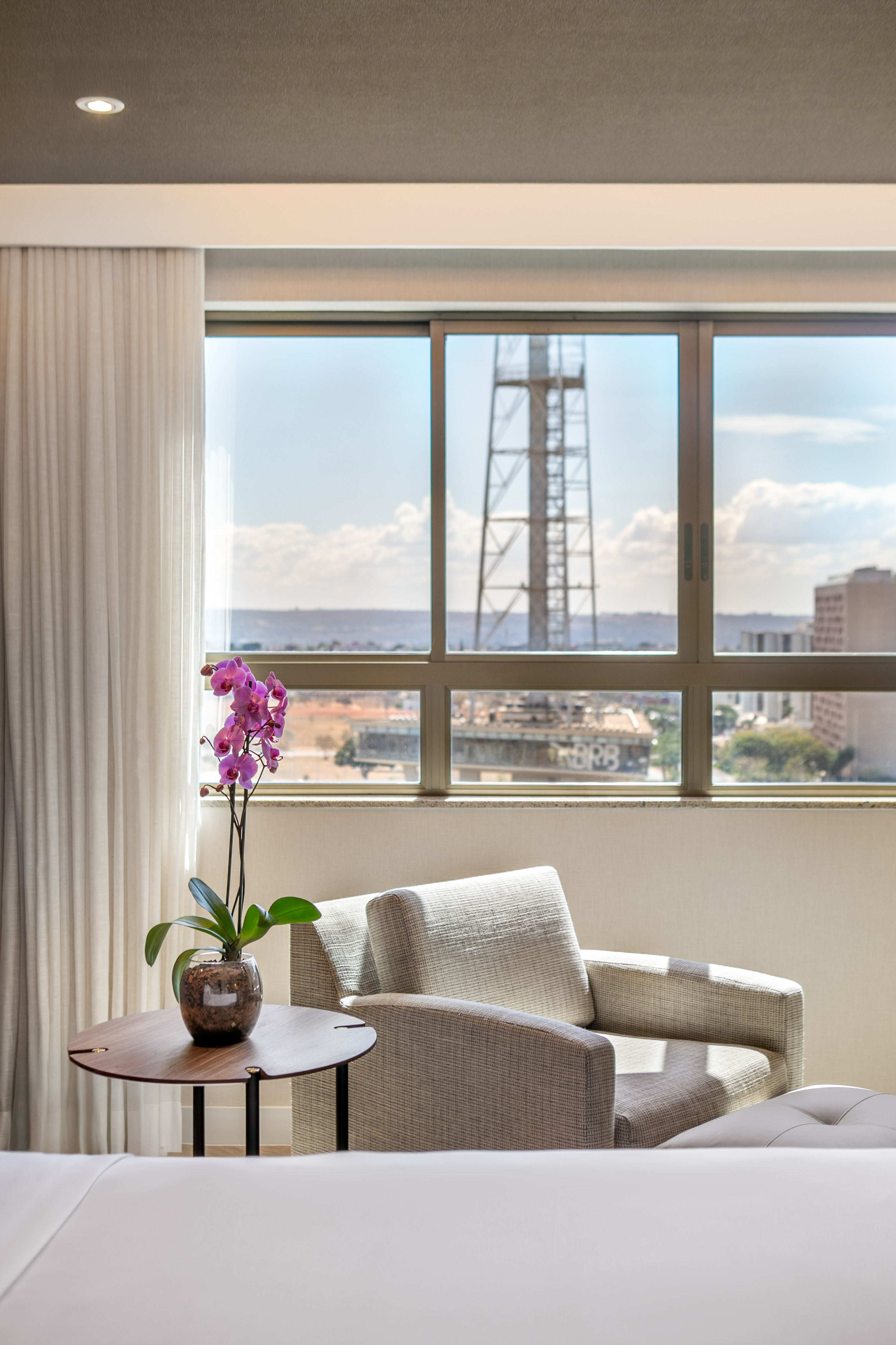 Hotel suite interior with city skyline view, purple orchid, and armchair.
