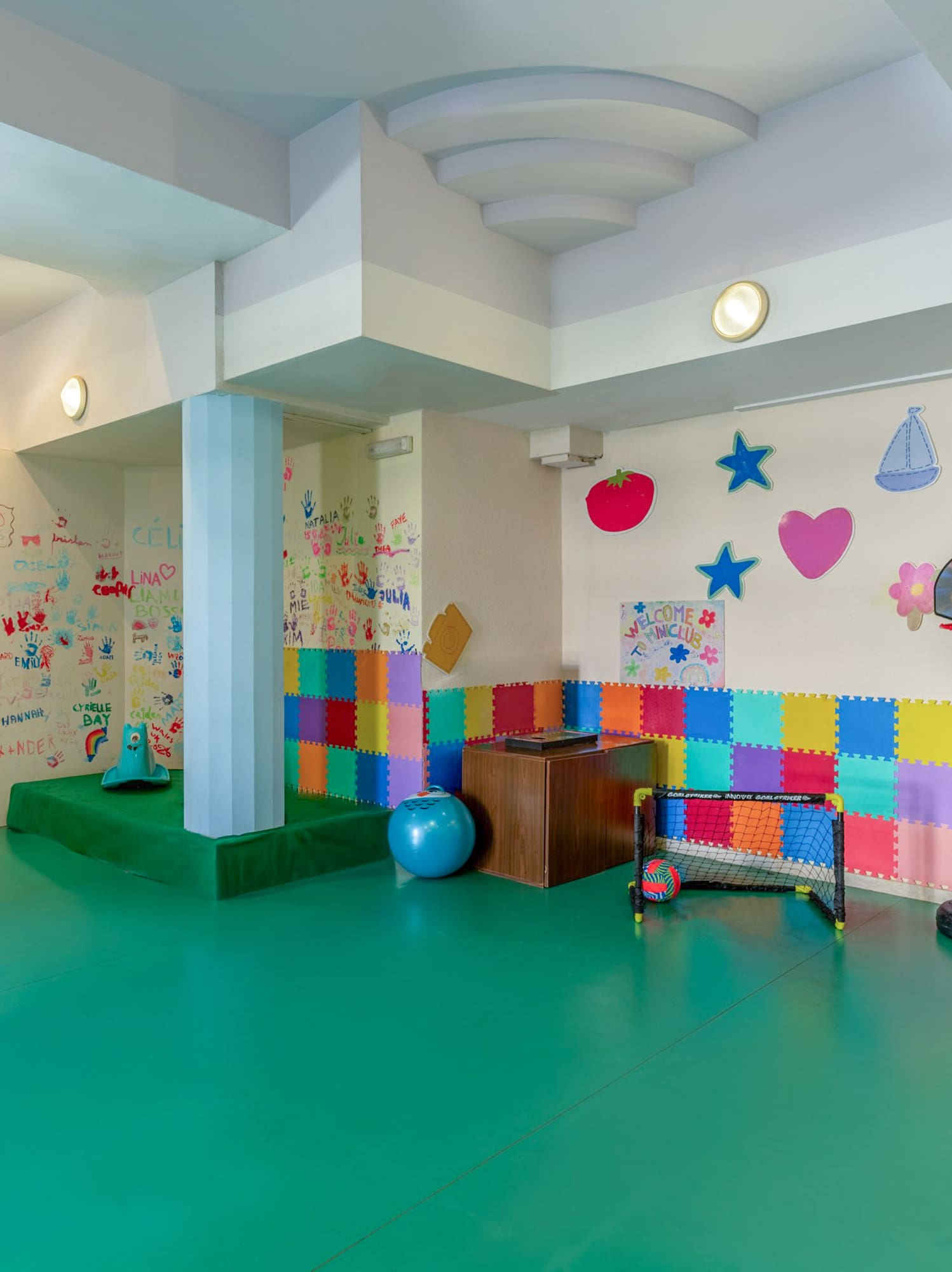 Kids' indoor playroom with green padded floor, art walls, basketball, soccer goal, and pool.
