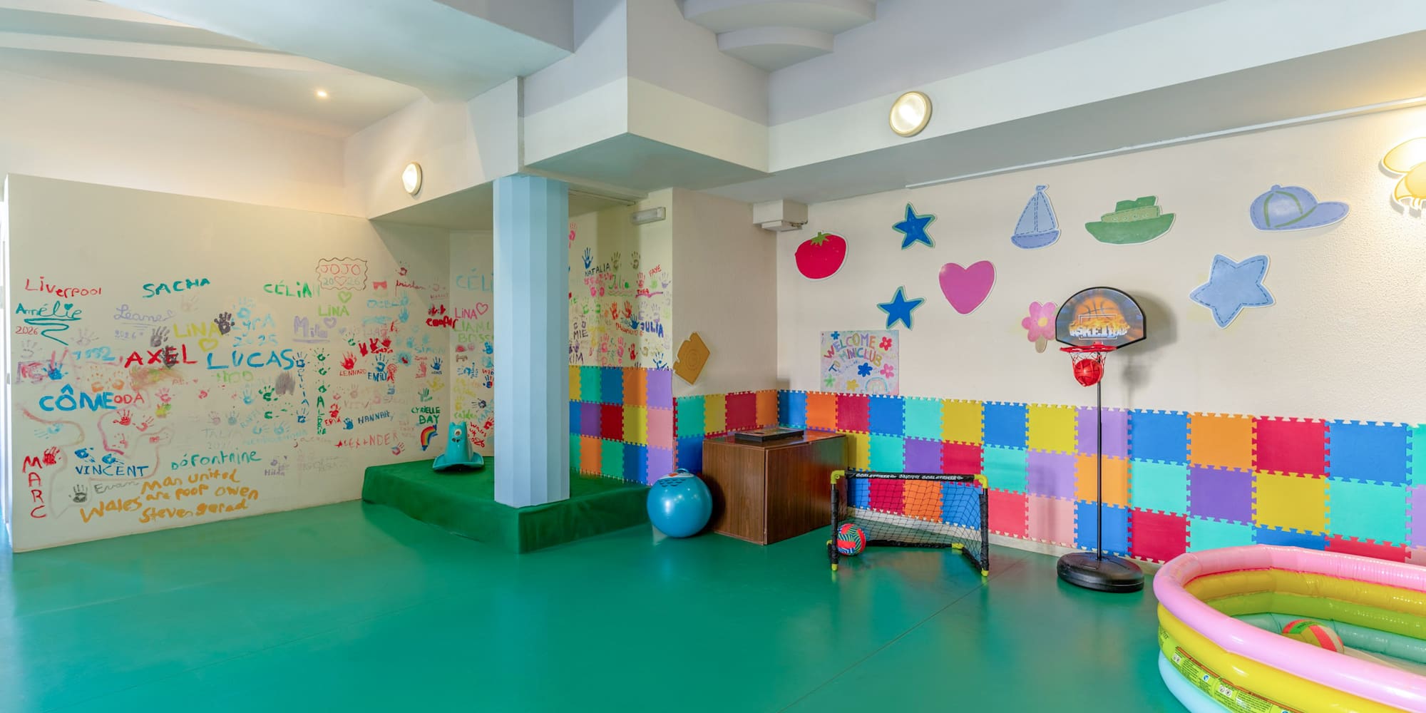 Colorful kids' playroom with green floor, artistic walls, soft mats, and toys.