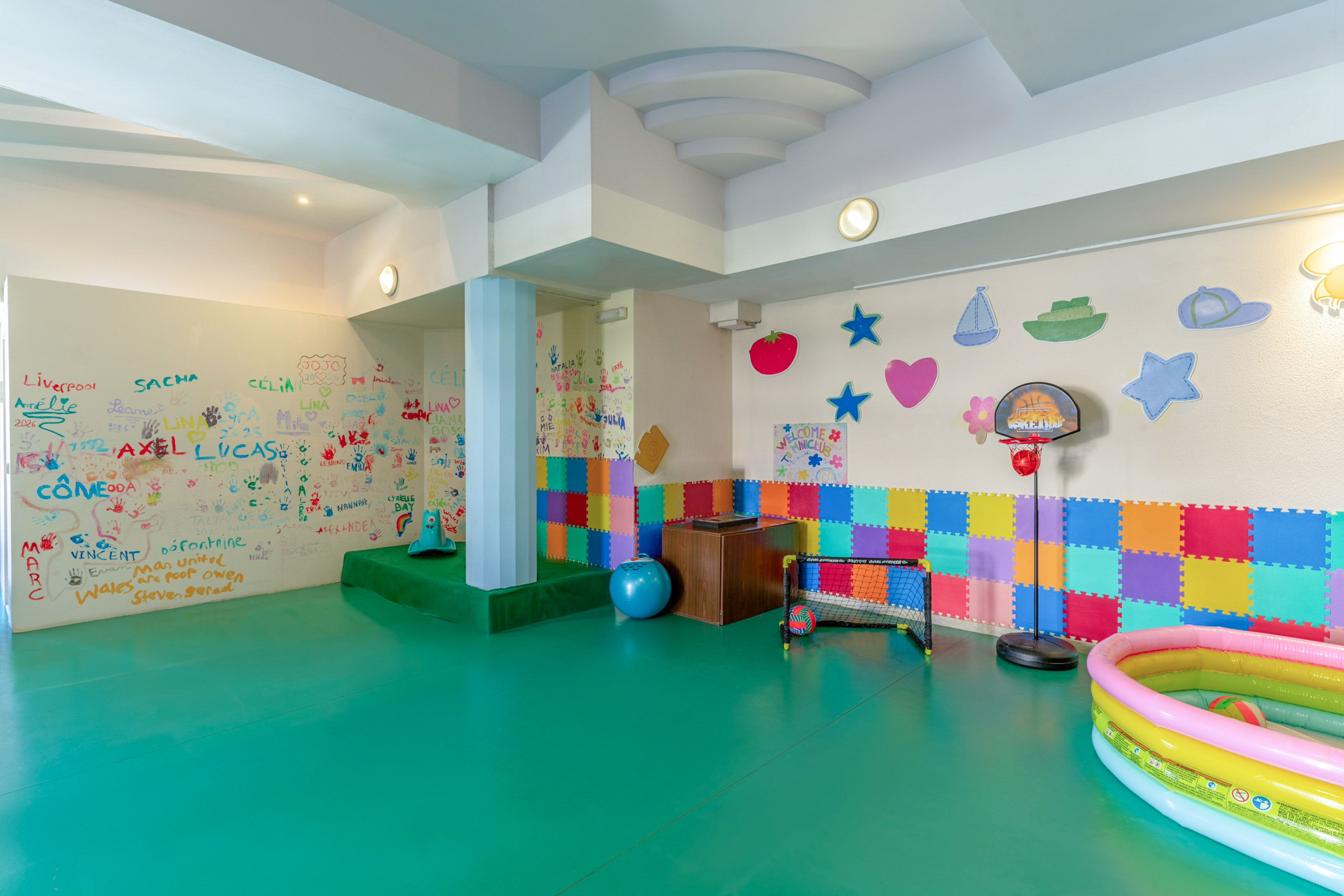 Colorful kids' playroom with green floor, artistic walls, soft mats, and toys.