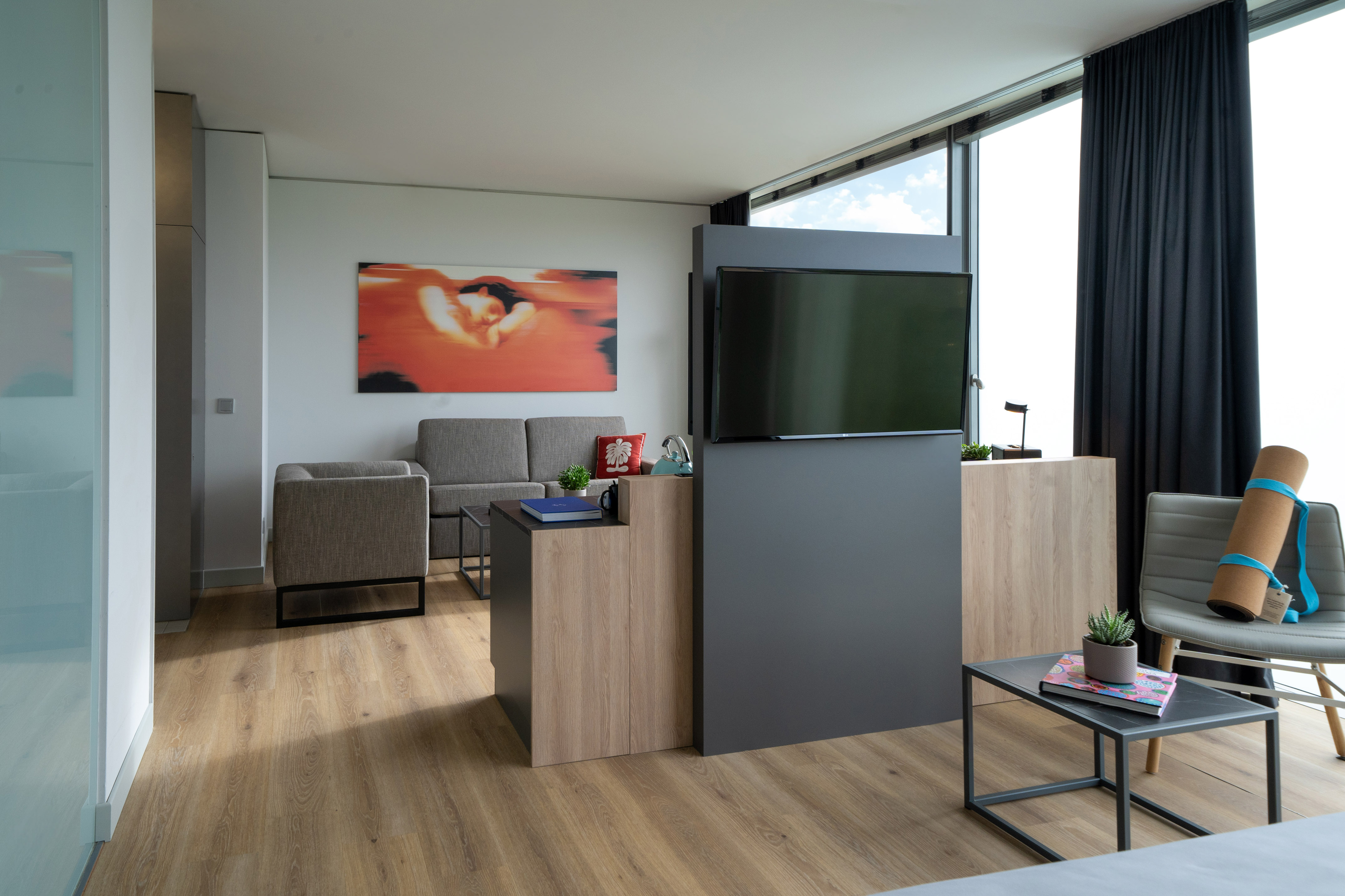 Modern hotel living room with TV, sofa, and yoga mat by large windows.