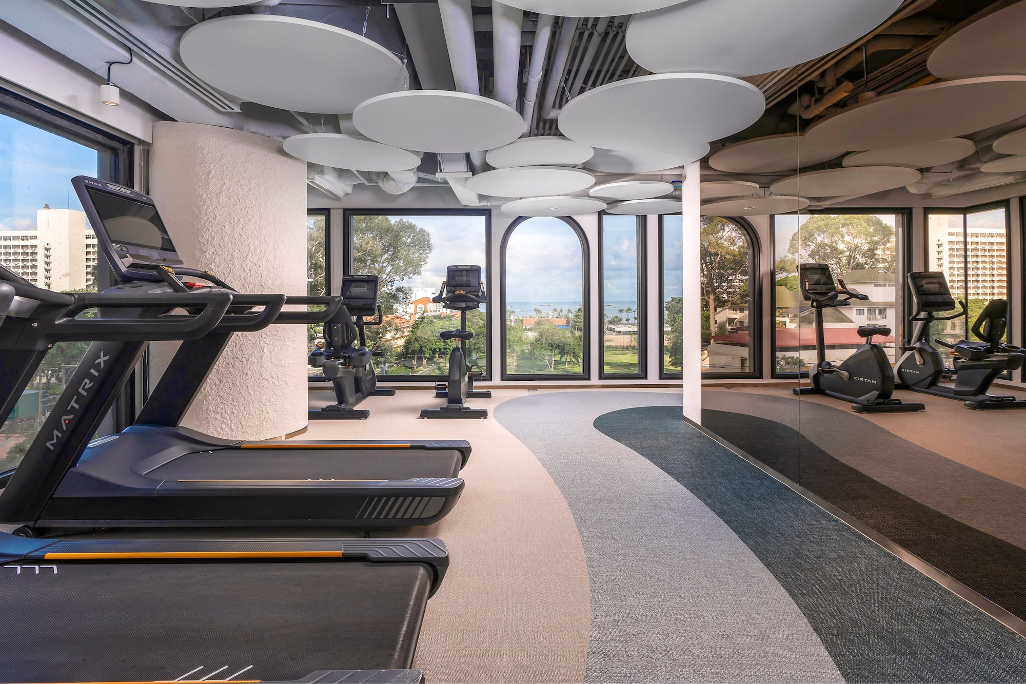 Bright modern gym with treadmills, exercise bikes, and large scenic windows.