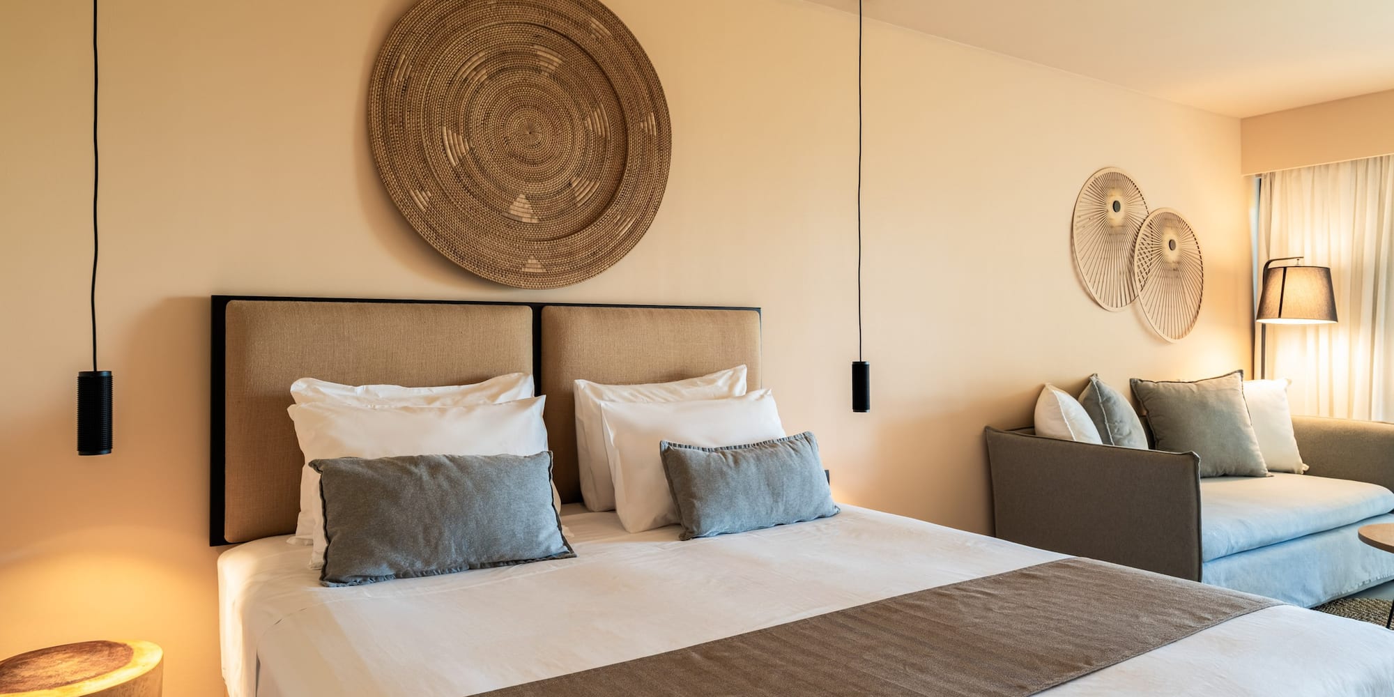 Neutral-toned modern bedroom with large bed, woven art, and sofa.