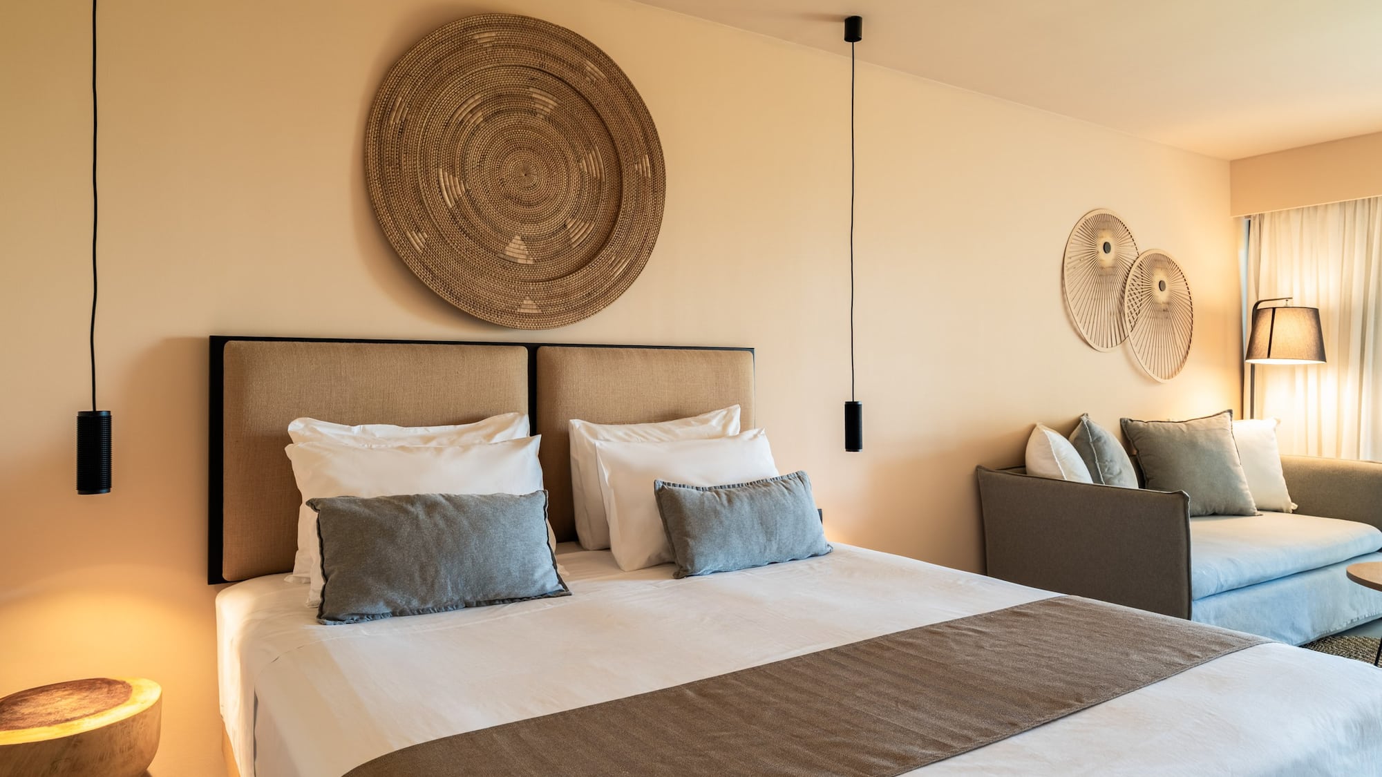 Neutral-toned modern bedroom with large bed, woven art, and sofa.