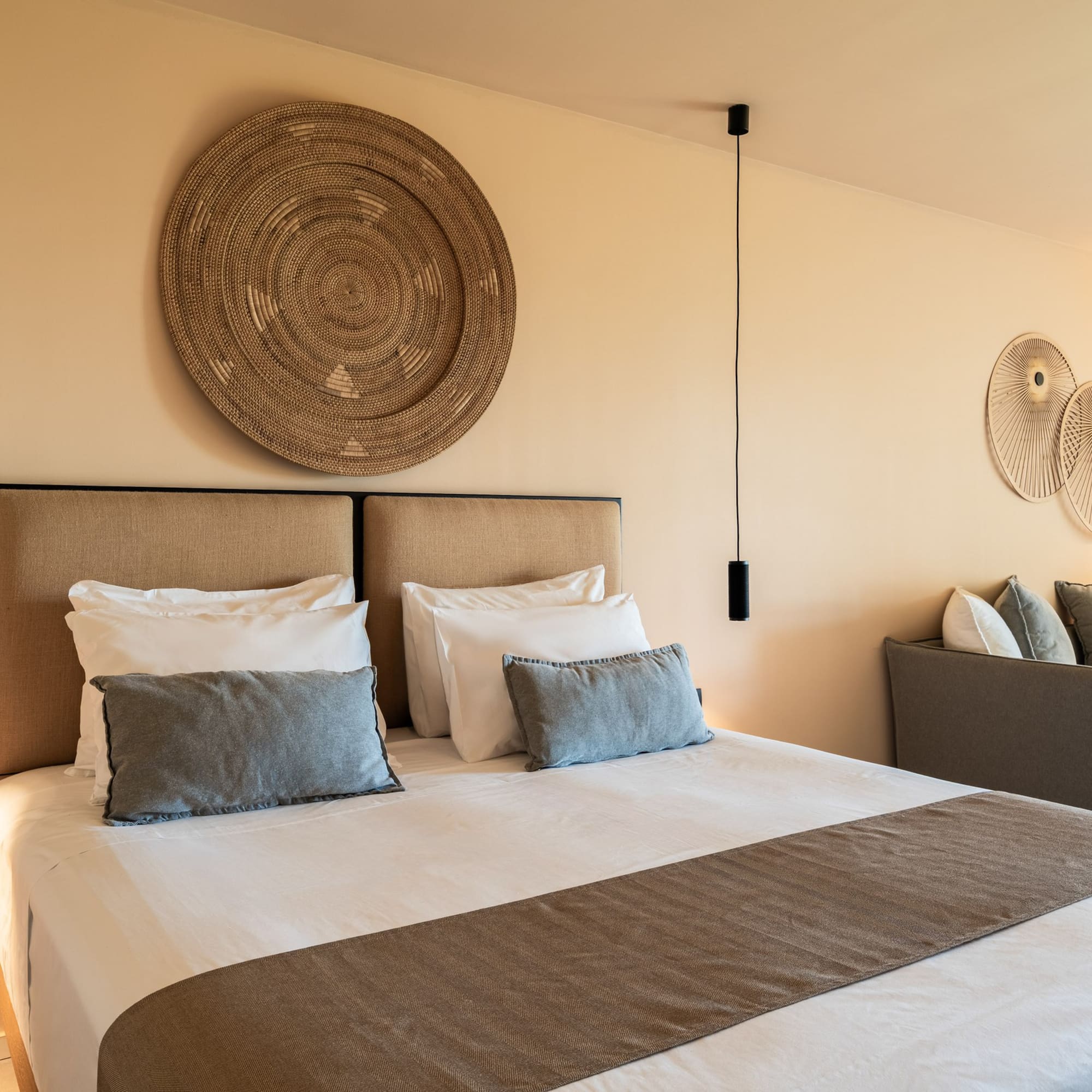 Neutral-toned modern bedroom with large bed, woven art, and sofa.