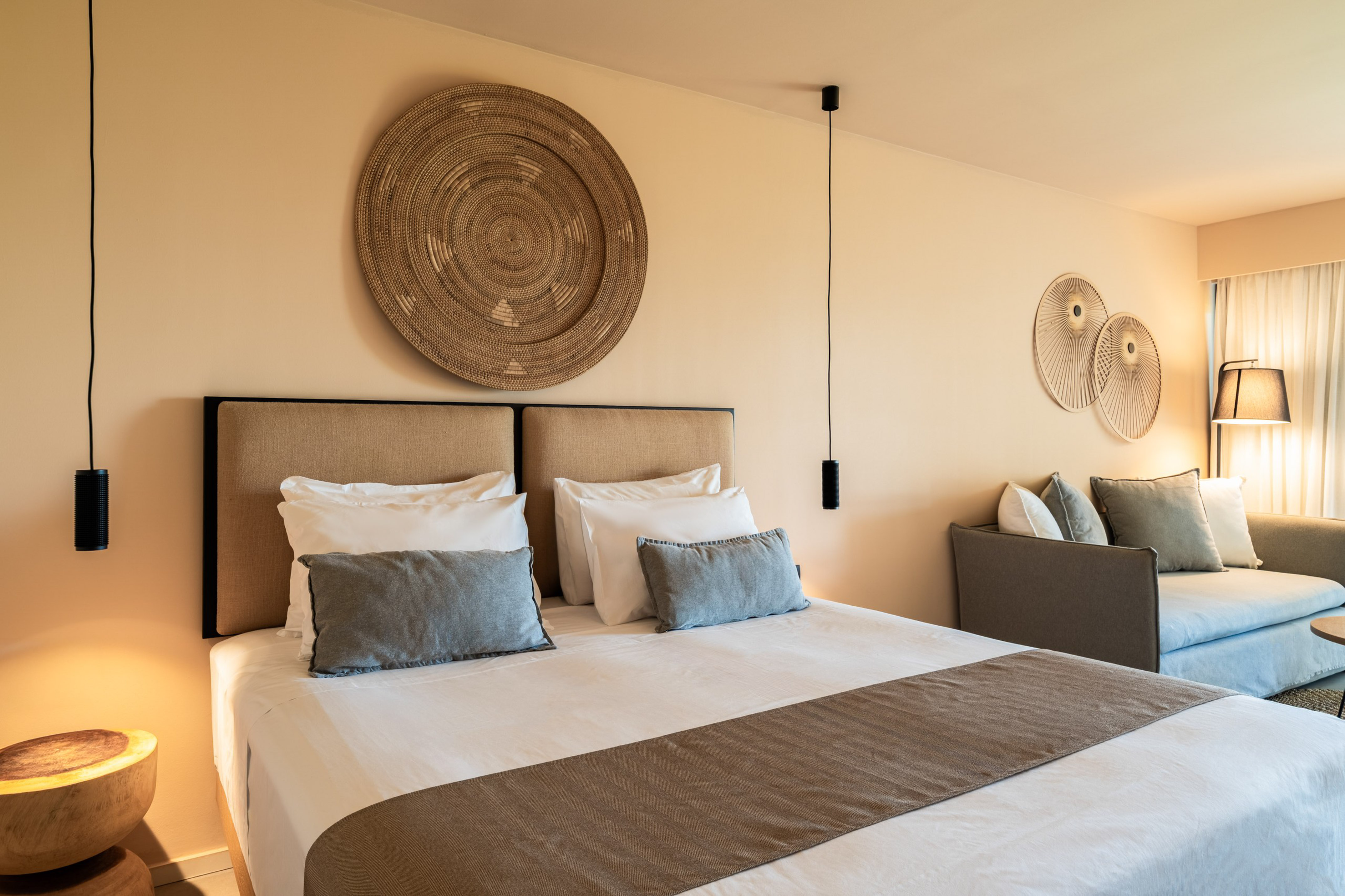 Neutral-toned modern bedroom with large bed, woven art, and sofa.