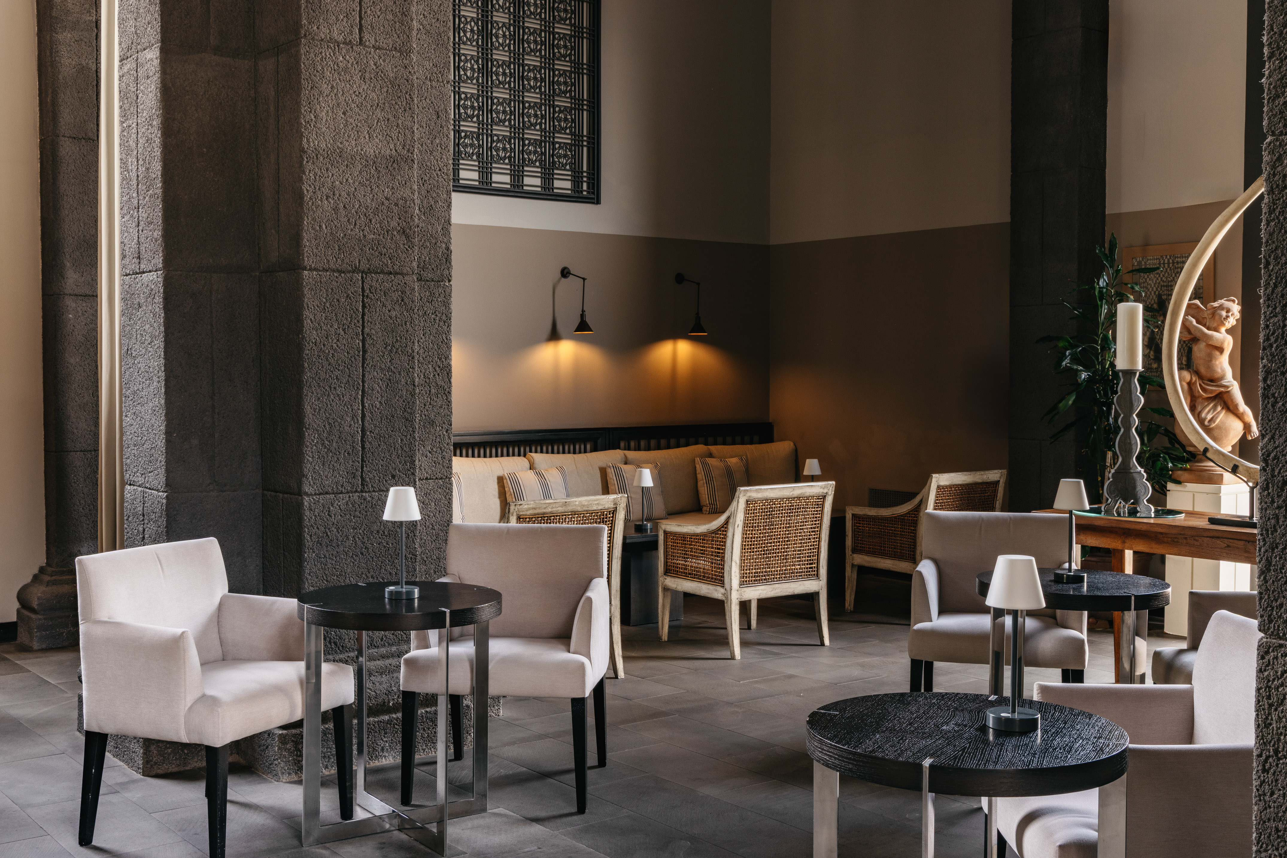 Cozy hotel lounge with stone columns, armchairs, dark tables, and warm lighting.