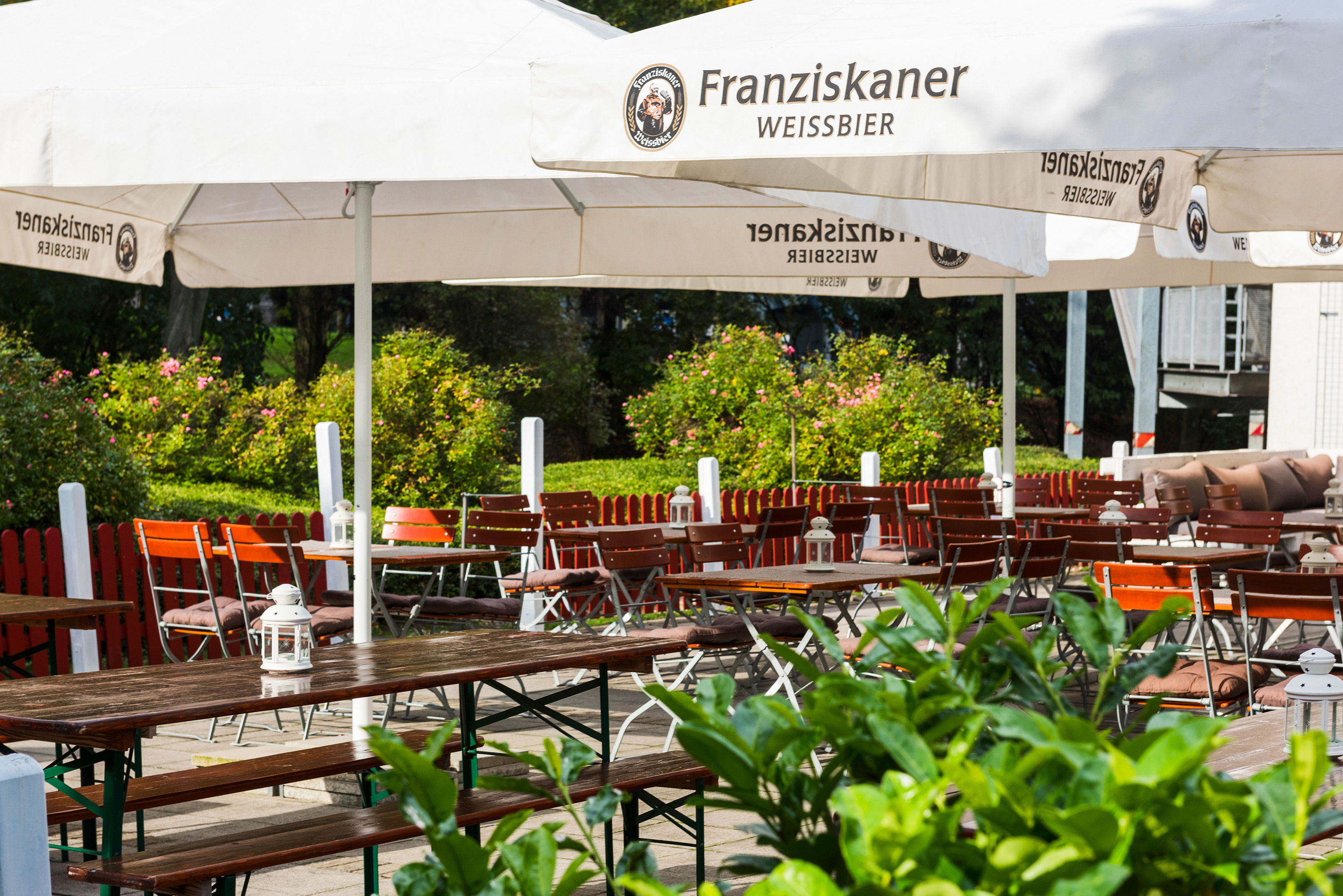 Franziskaner beer garden with white branded umbrellas and outdoor seating.