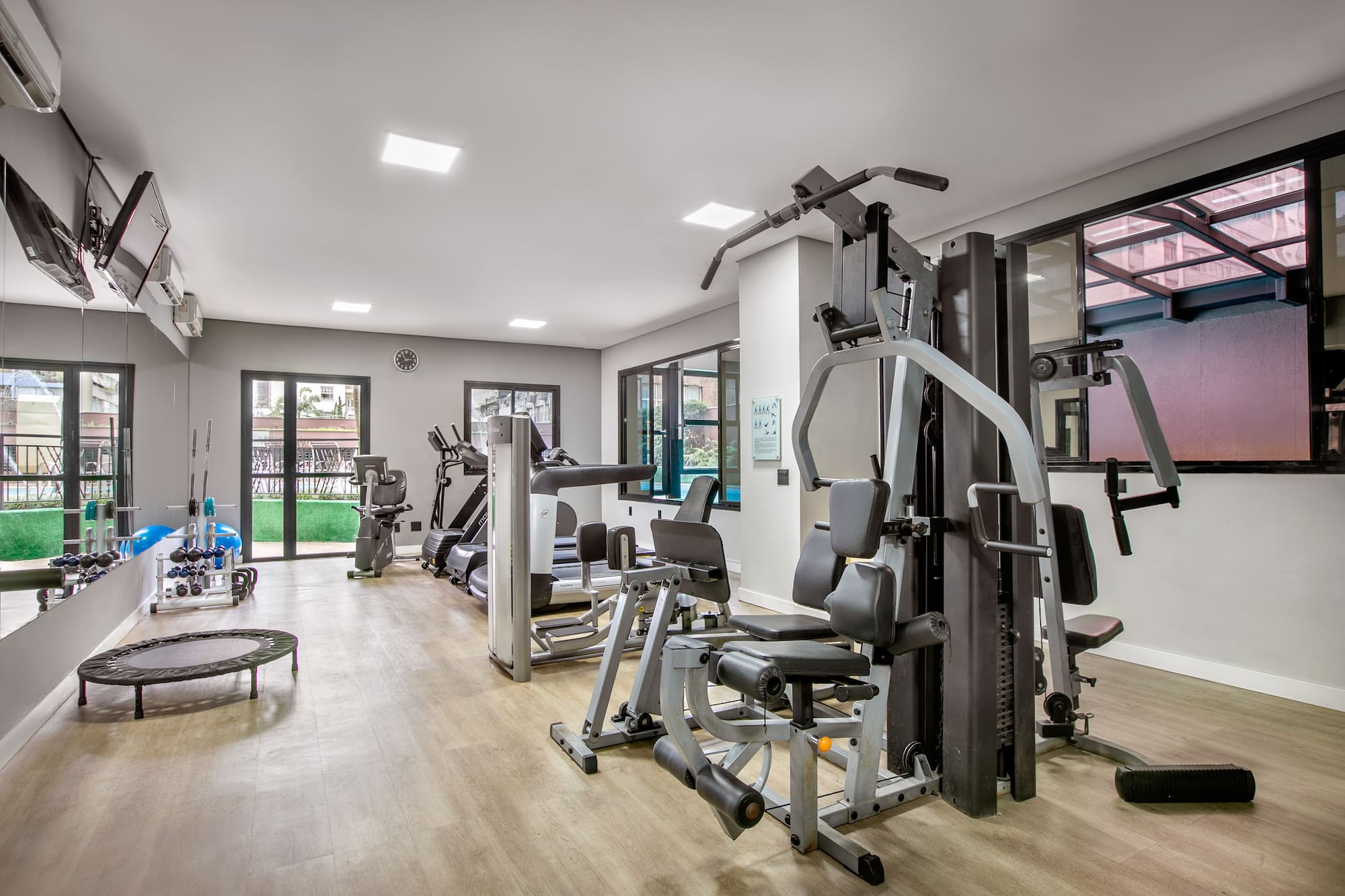 Spacious gym with diverse fitness equipment, wooden floor, and natural light.