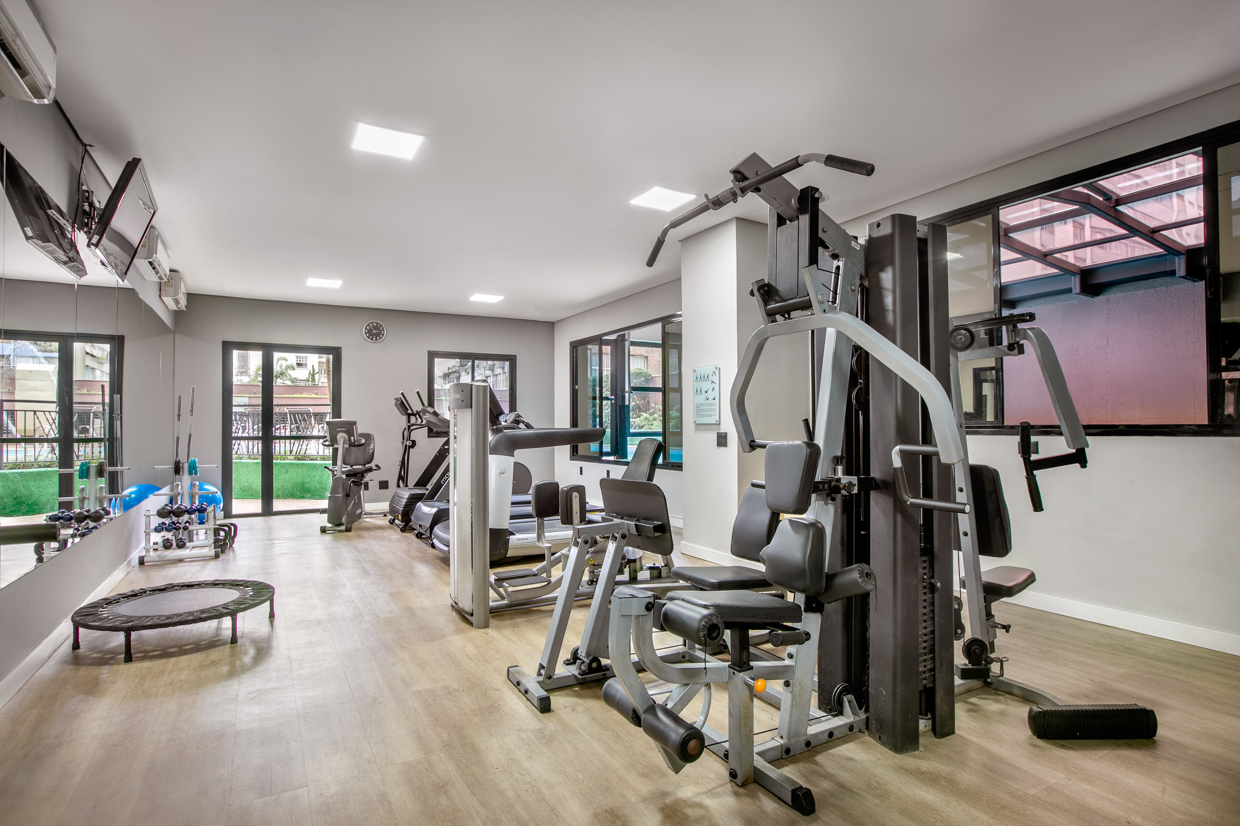 Spacious gym with diverse fitness equipment, wooden floor, and natural light.