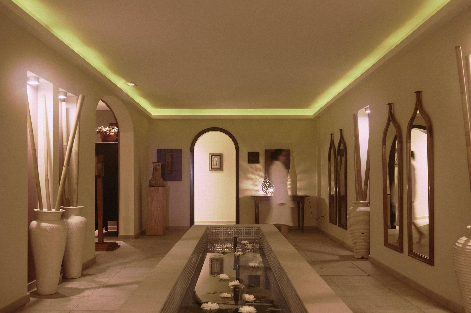 Spa hallway with water feature, floating white flowers, and warm cove lighting.