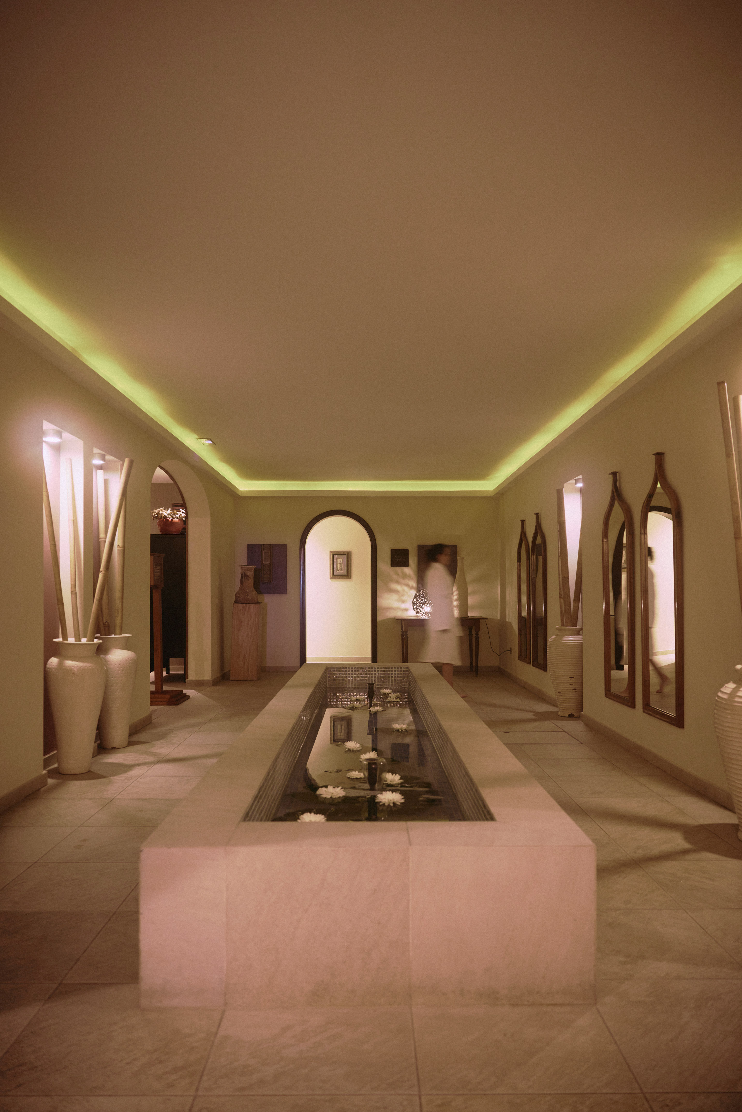 Spa hallway with water feature, floating white flowers, and warm cove lighting.