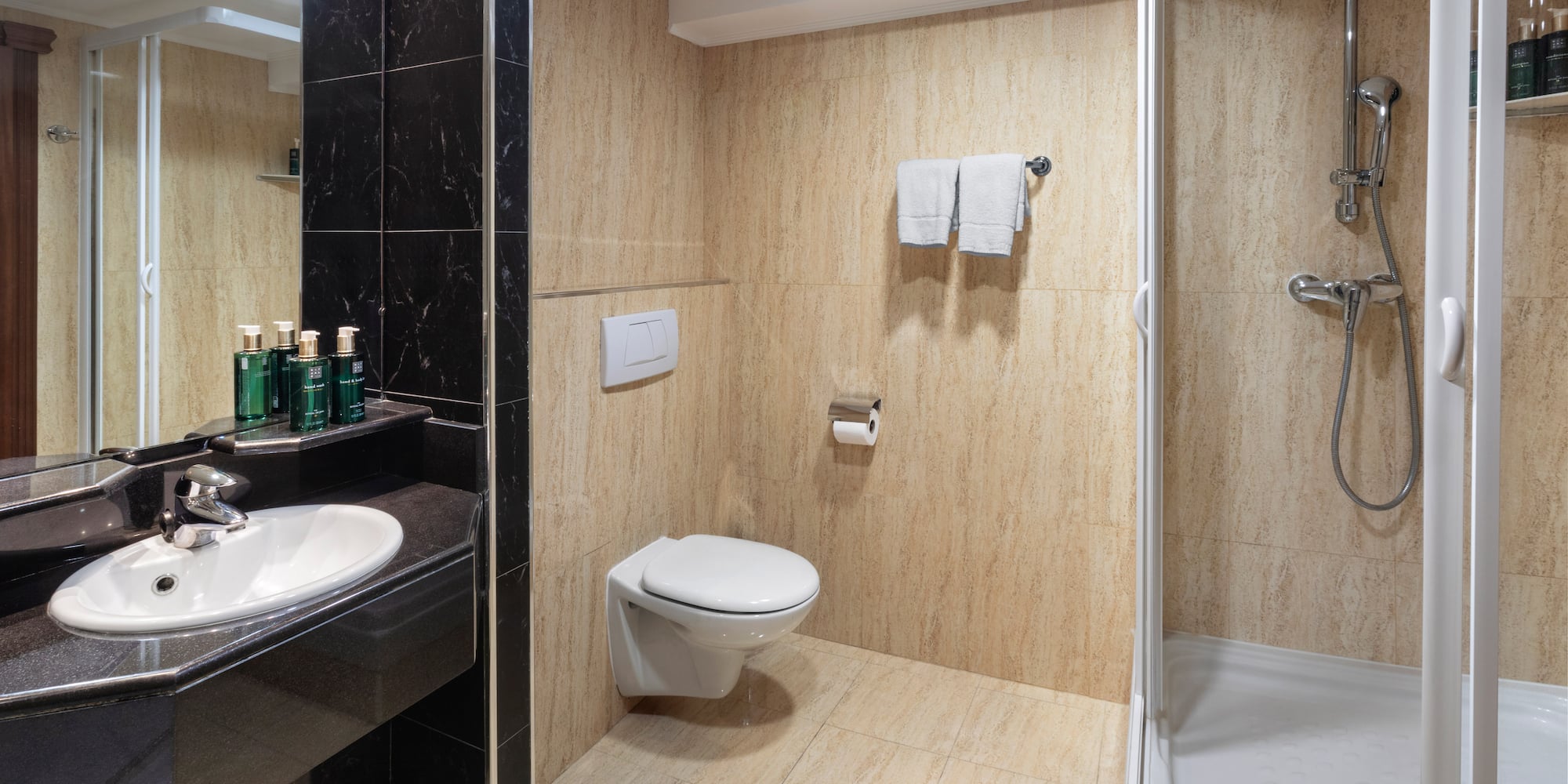 Modern hotel bathroom with black marble vanity, white sink, toilet, and glass shower.