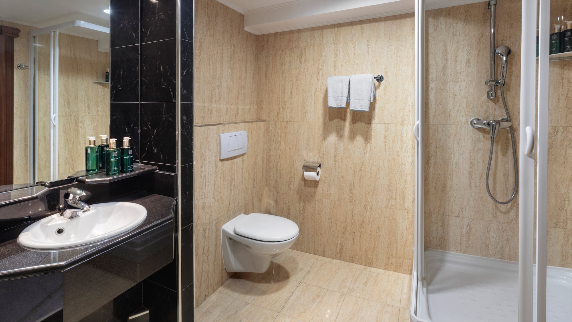 Modern hotel bathroom with black marble vanity, white sink, toilet, and glass shower.
