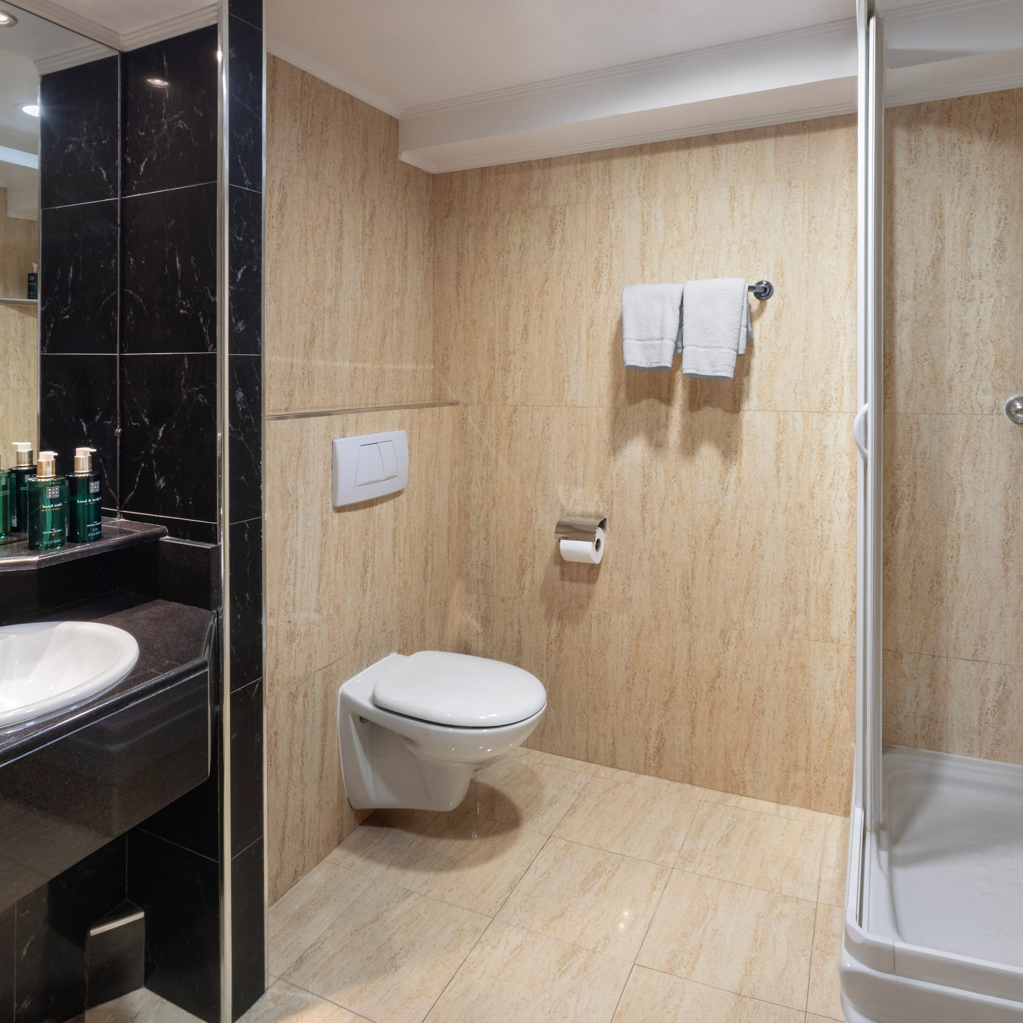 Modern hotel bathroom with black marble vanity, white sink, toilet, and glass shower.