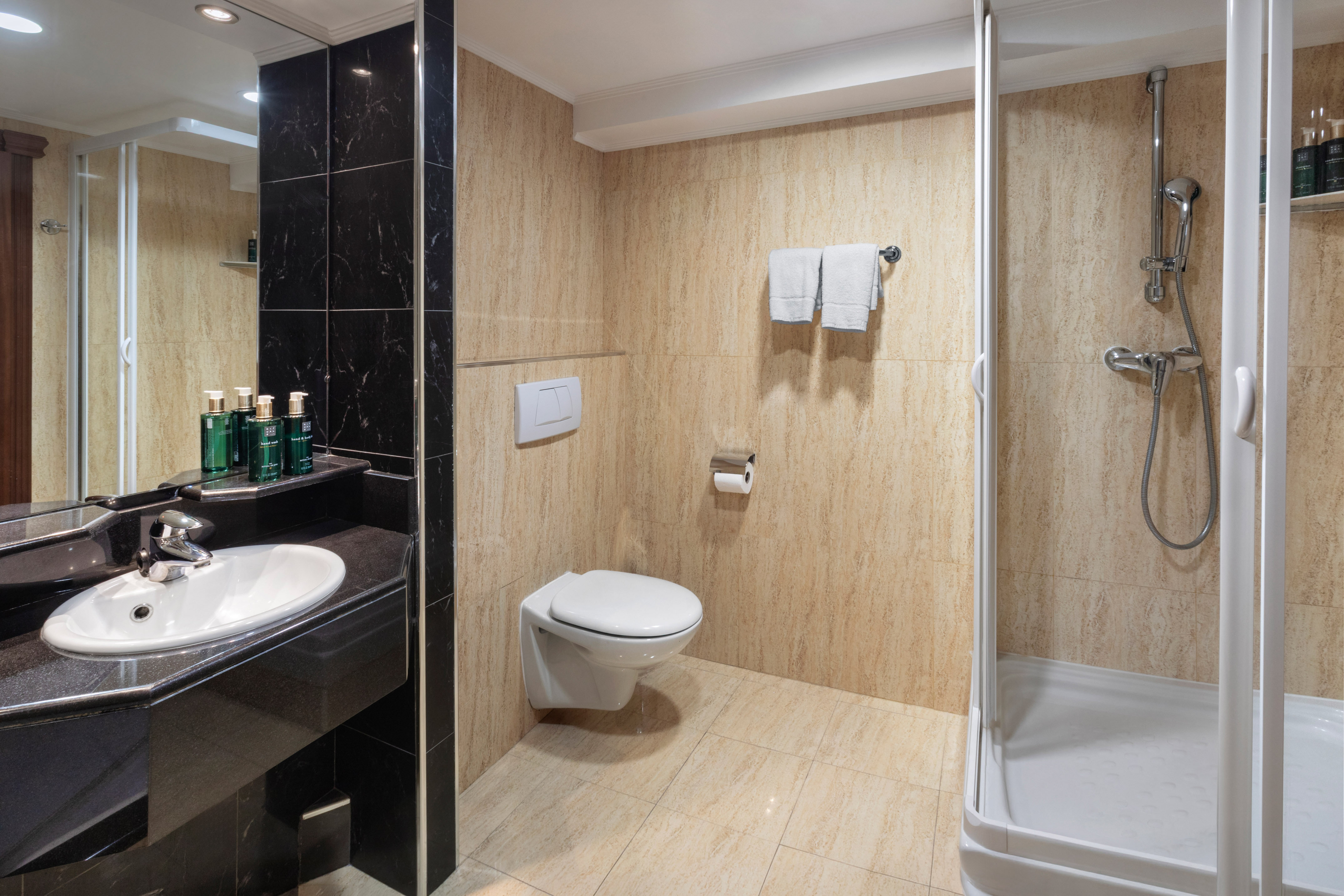 Modern hotel bathroom with black marble vanity, white sink, toilet, and glass shower.
