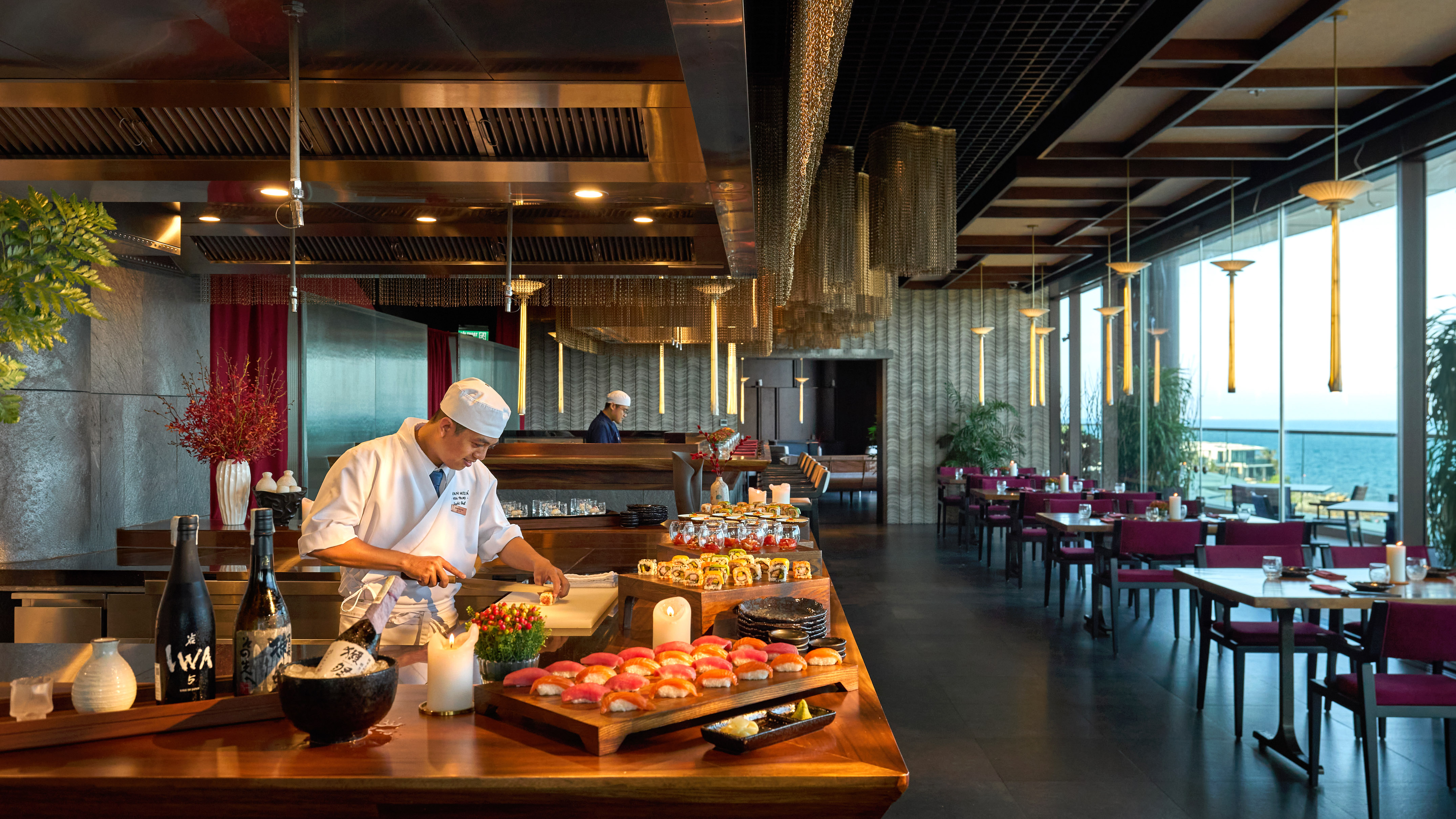 Chef preparing sushi and sashimi at a modern Japanese restaurant with ocean view.