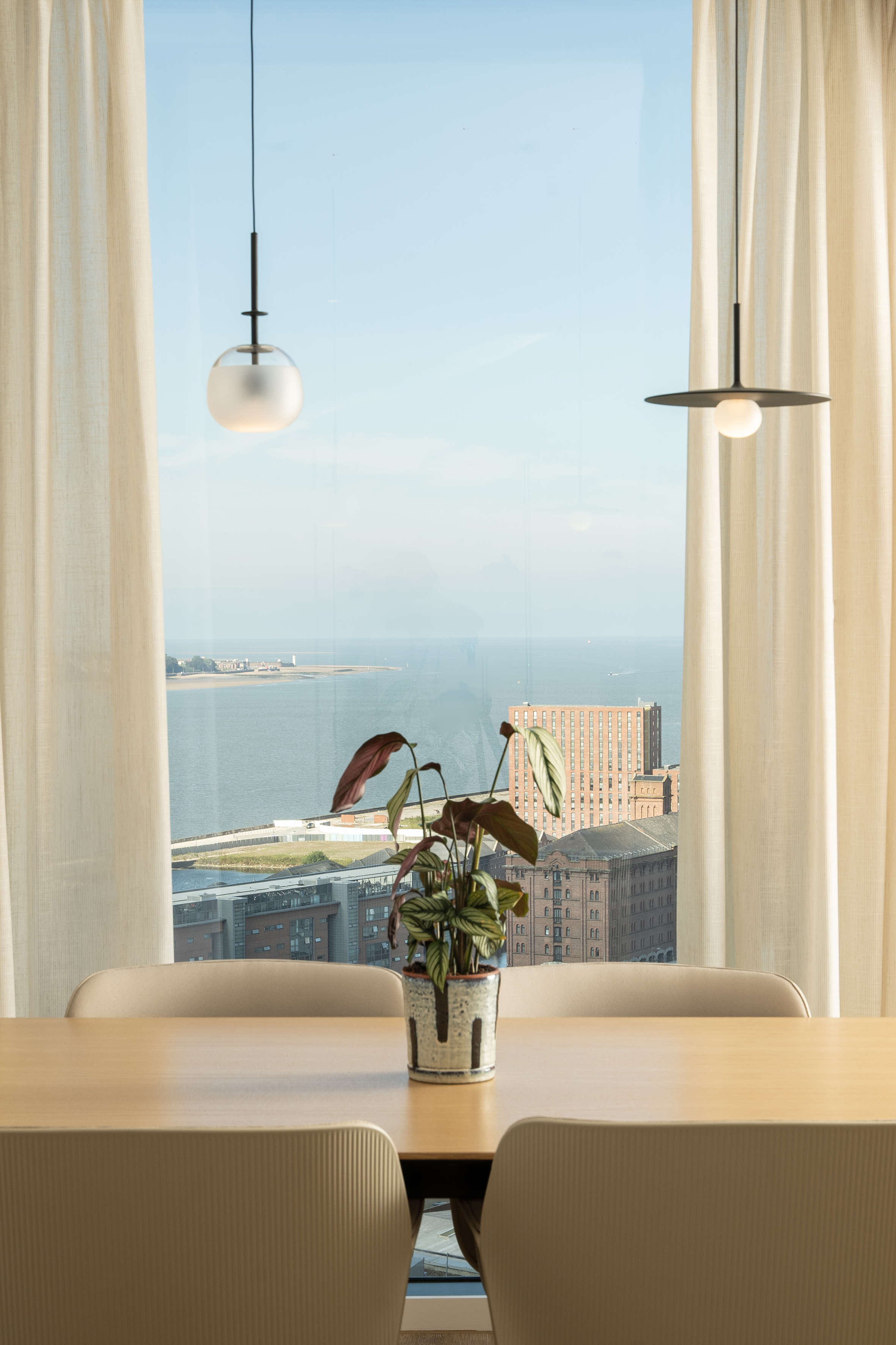 Modern interior with sea & city view, dining table, plant, and pendant lights.